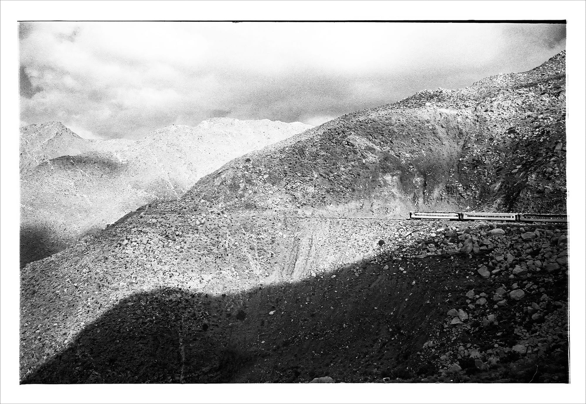 Black and white photo of a train traveling through a rugged mountainous landscape.