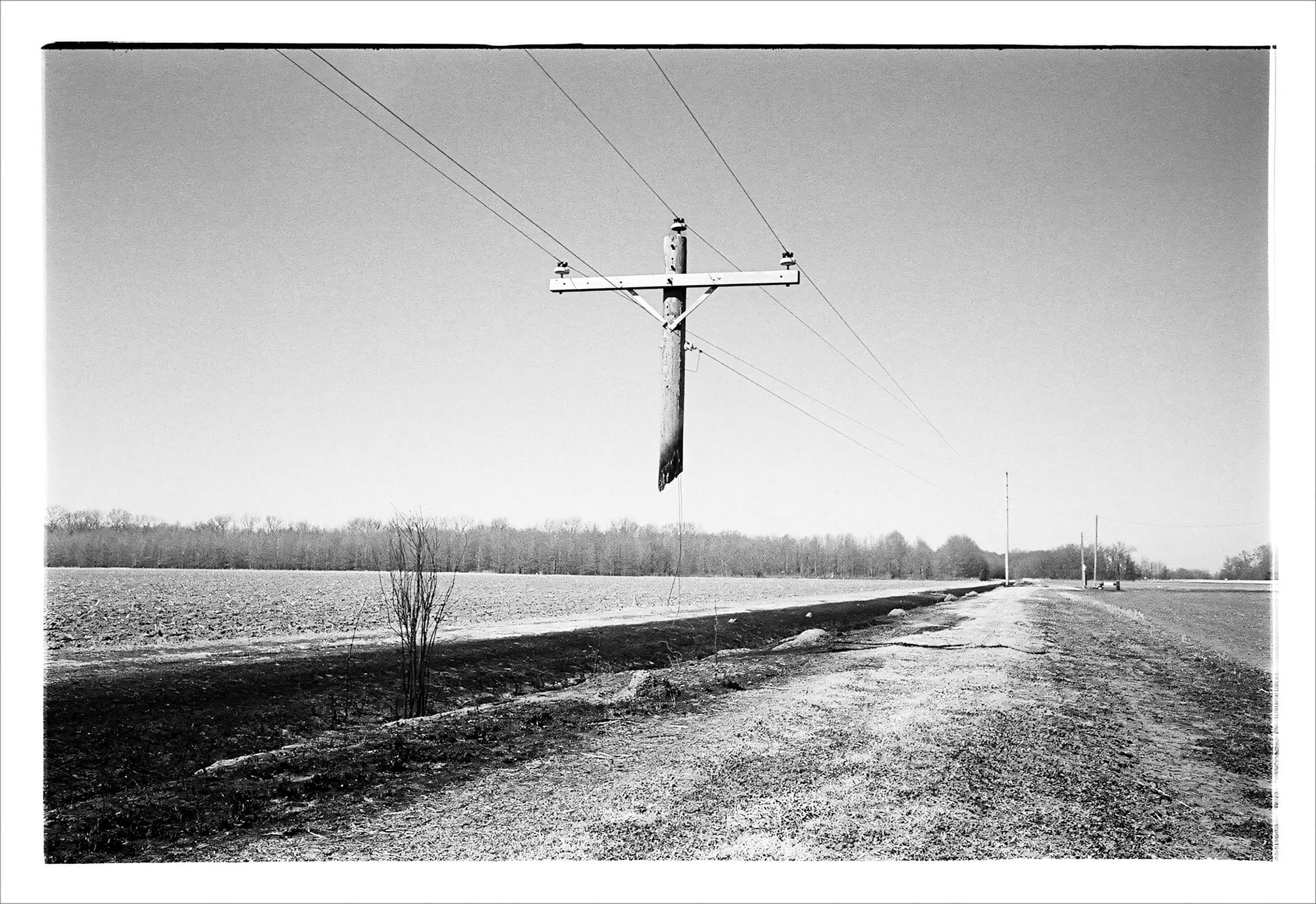 Black and white photo of a broken power pole hanging as a cross in a rural landscape.
