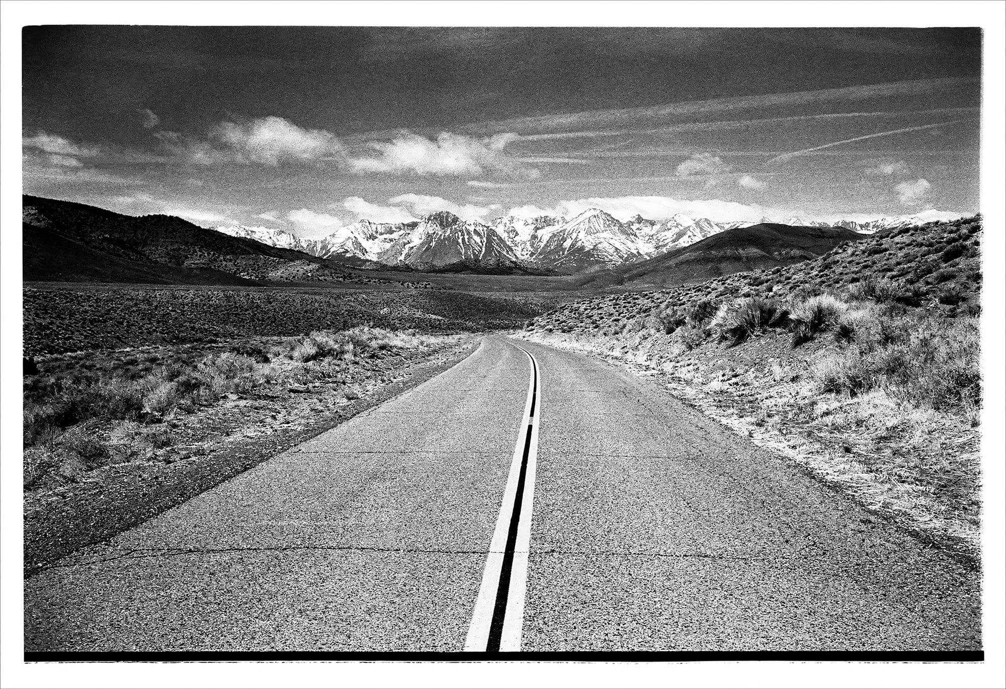 Black and white photo of a winding road leading to snow-capped mountains.