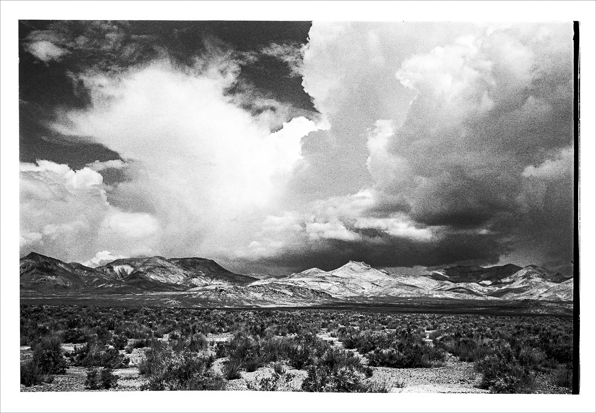 Monochrome image of a stormy sky above a barren, hilly terrain.