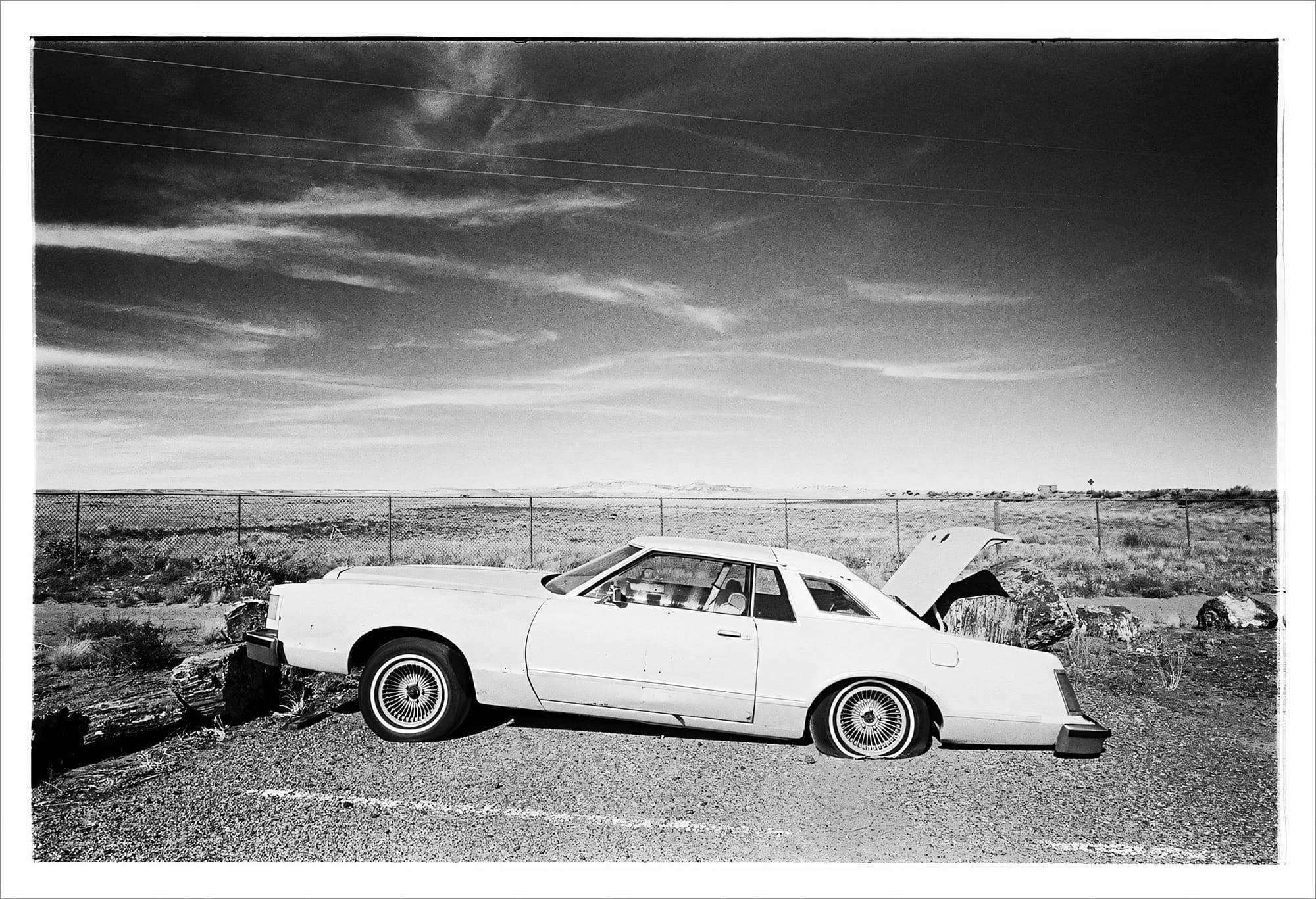 Classic car with custom wheels in an open, arid field.