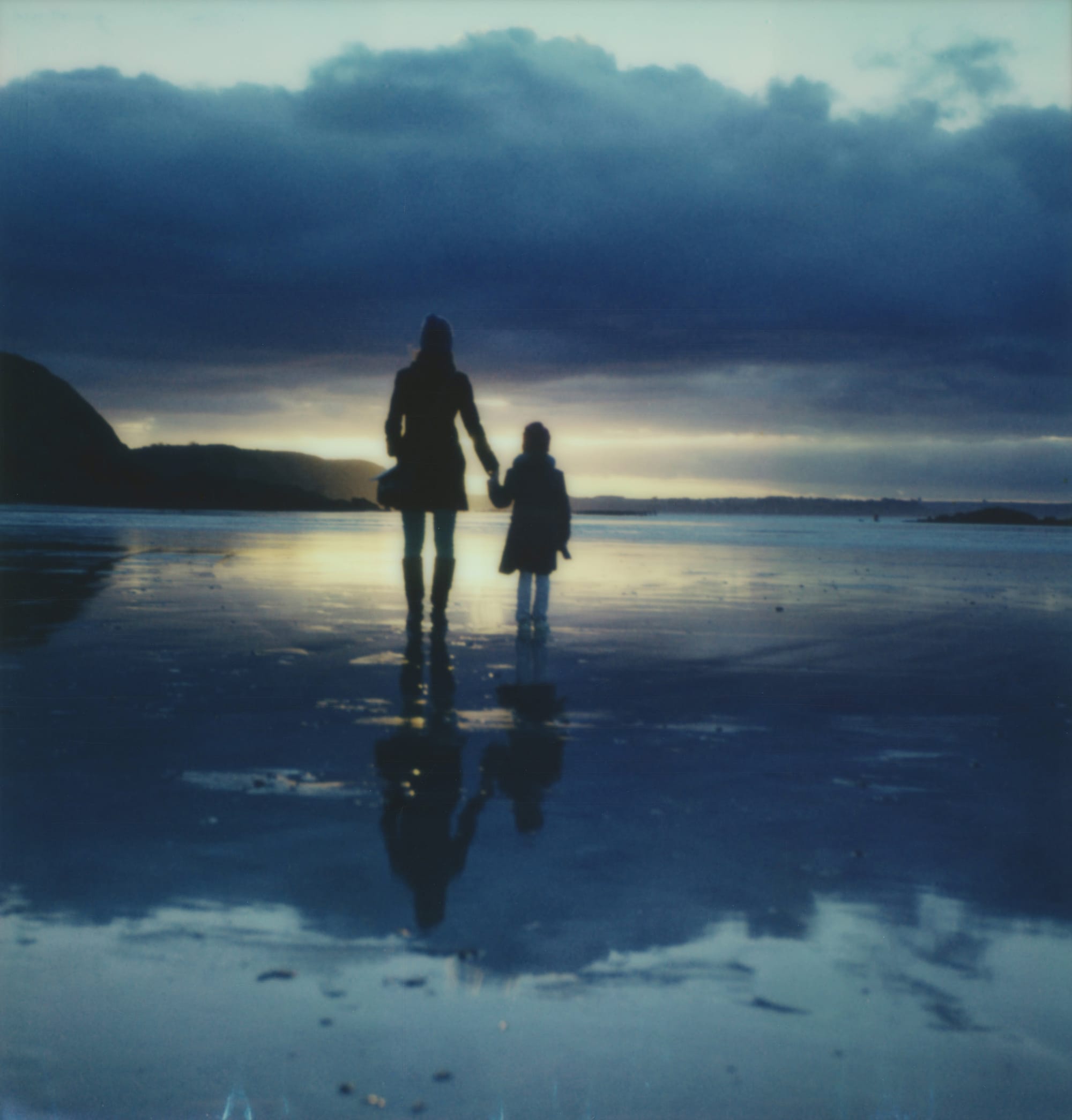 Woman and child silhouetted on beach at sunset with storm clouds.