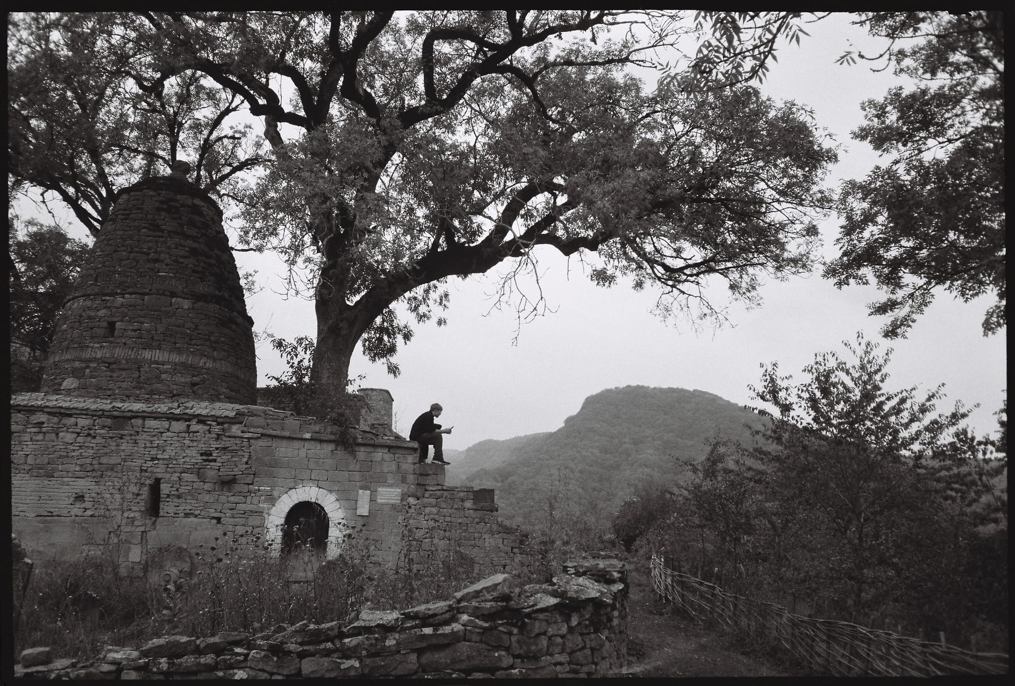Man sitting on ancient stone ruins with a mountain in the background.