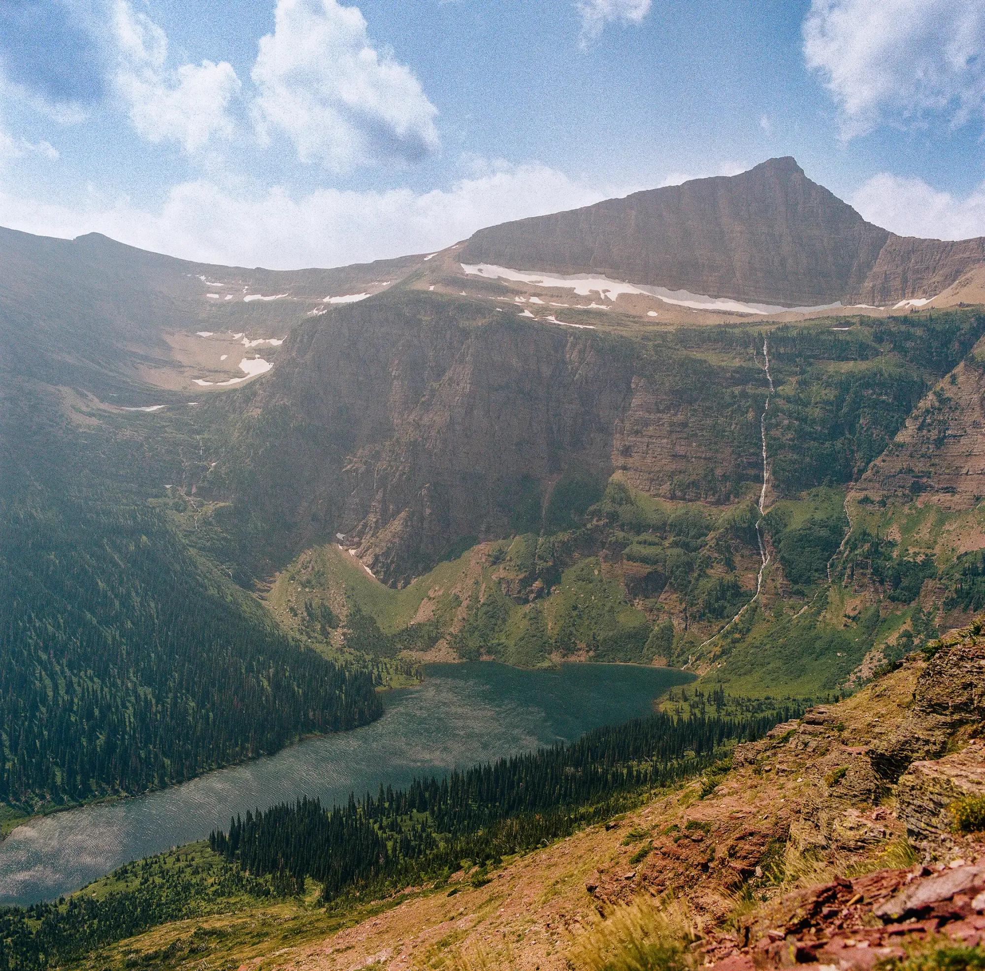 Alpine lake surrounded by peaks and conifer forest on film.