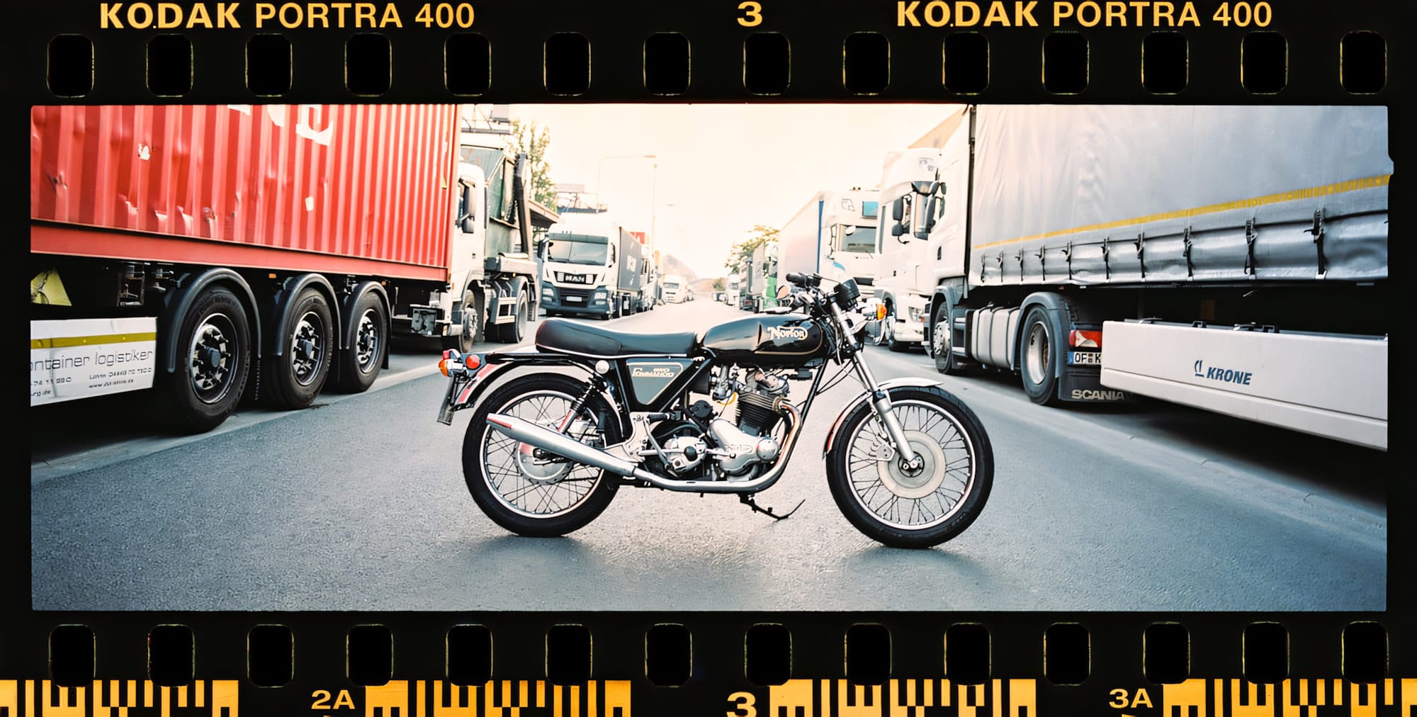 A vintage motorcycle parked on a road surrounded by large trucks.