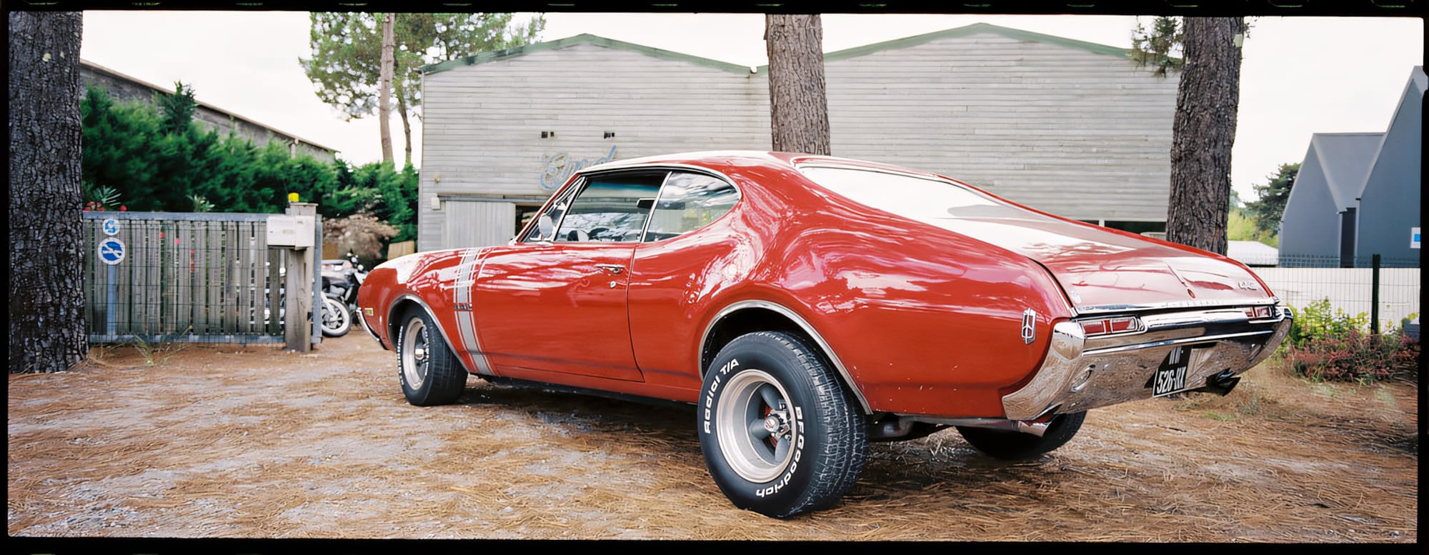 A red vintage Pontiac GTO parked on a driveway in a rural area.
