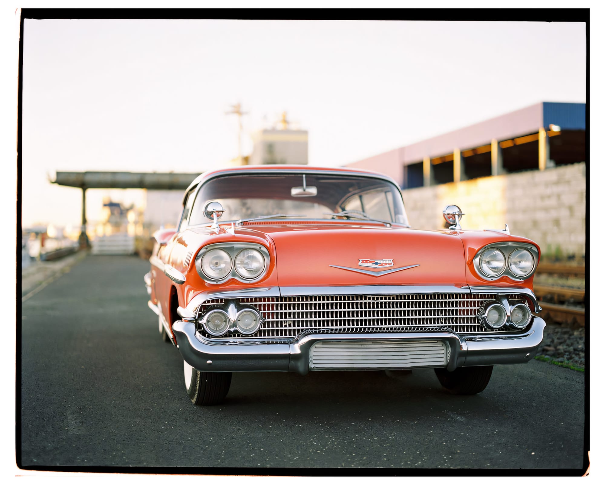 A classic red car with chrome details and dual headlights, parked outdoors.