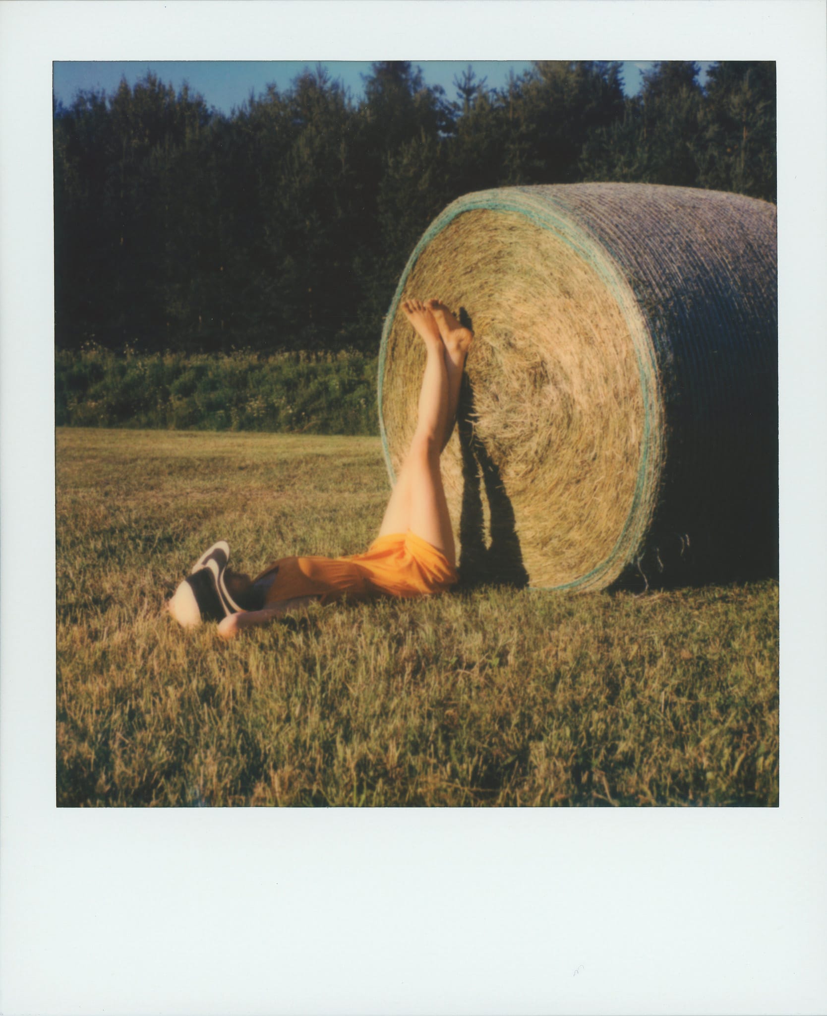 Young woman relaxing against hay bale in summer field on Polaroid.