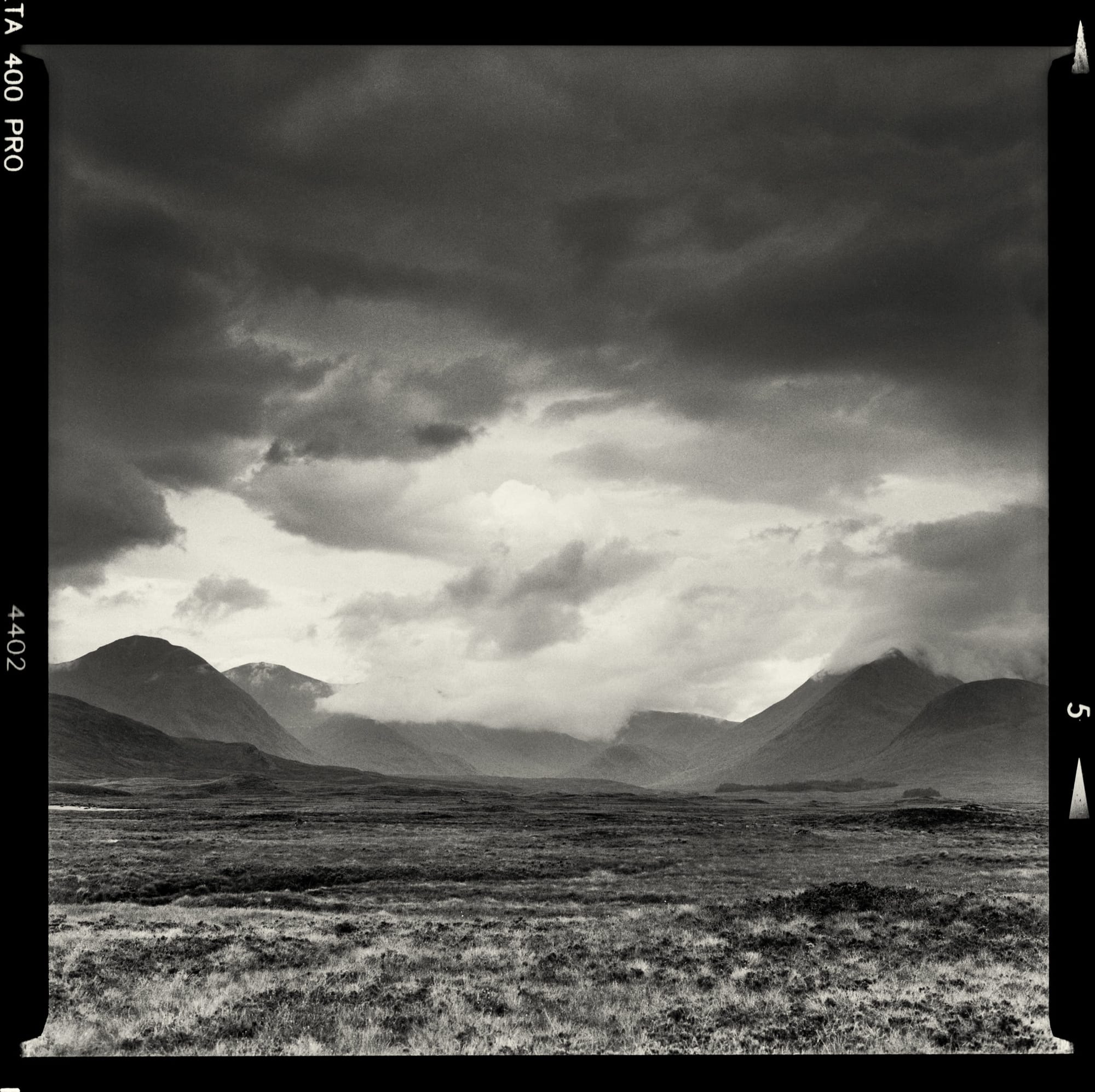 Expansive plain under a stormy sky with a mountain range in the background.