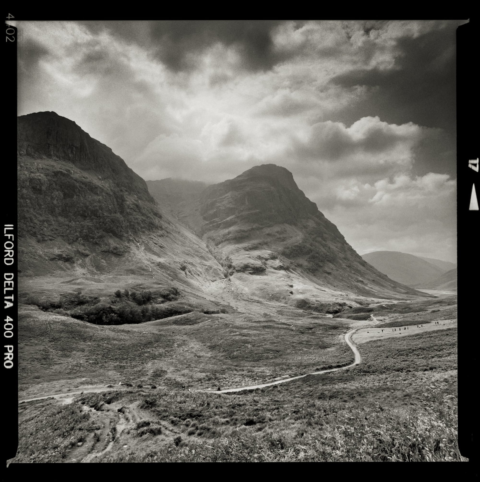A winding mountain road alongside rugged hills with dramatic skies above.