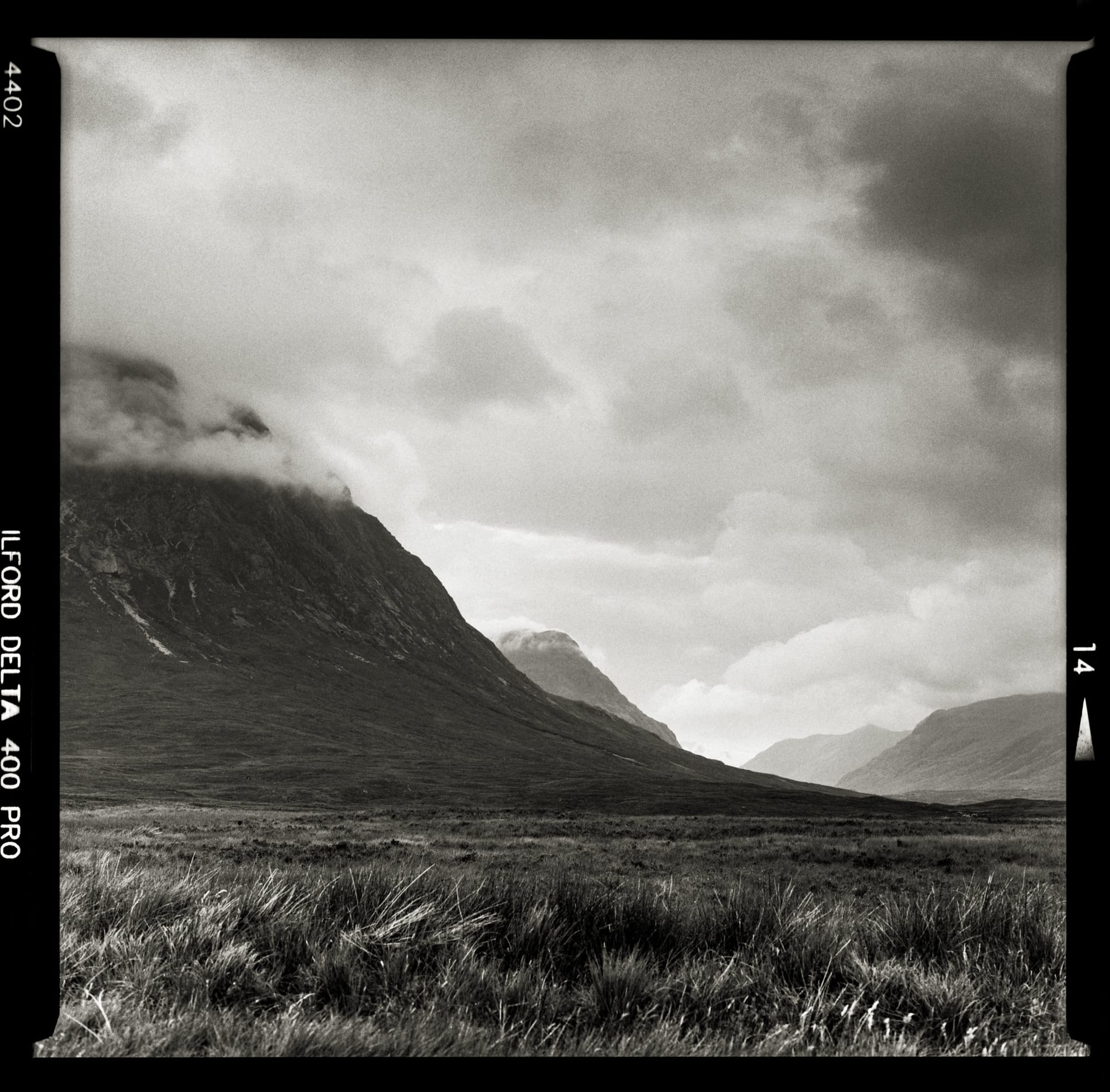 Rugged mountain scene with low-hanging clouds and grassy terrain.