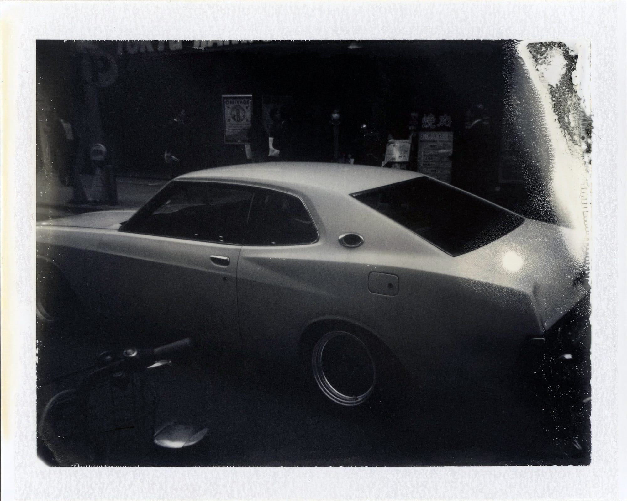 1970s muscle car coupe with spoiler photographed on polaroid in a dark setting.