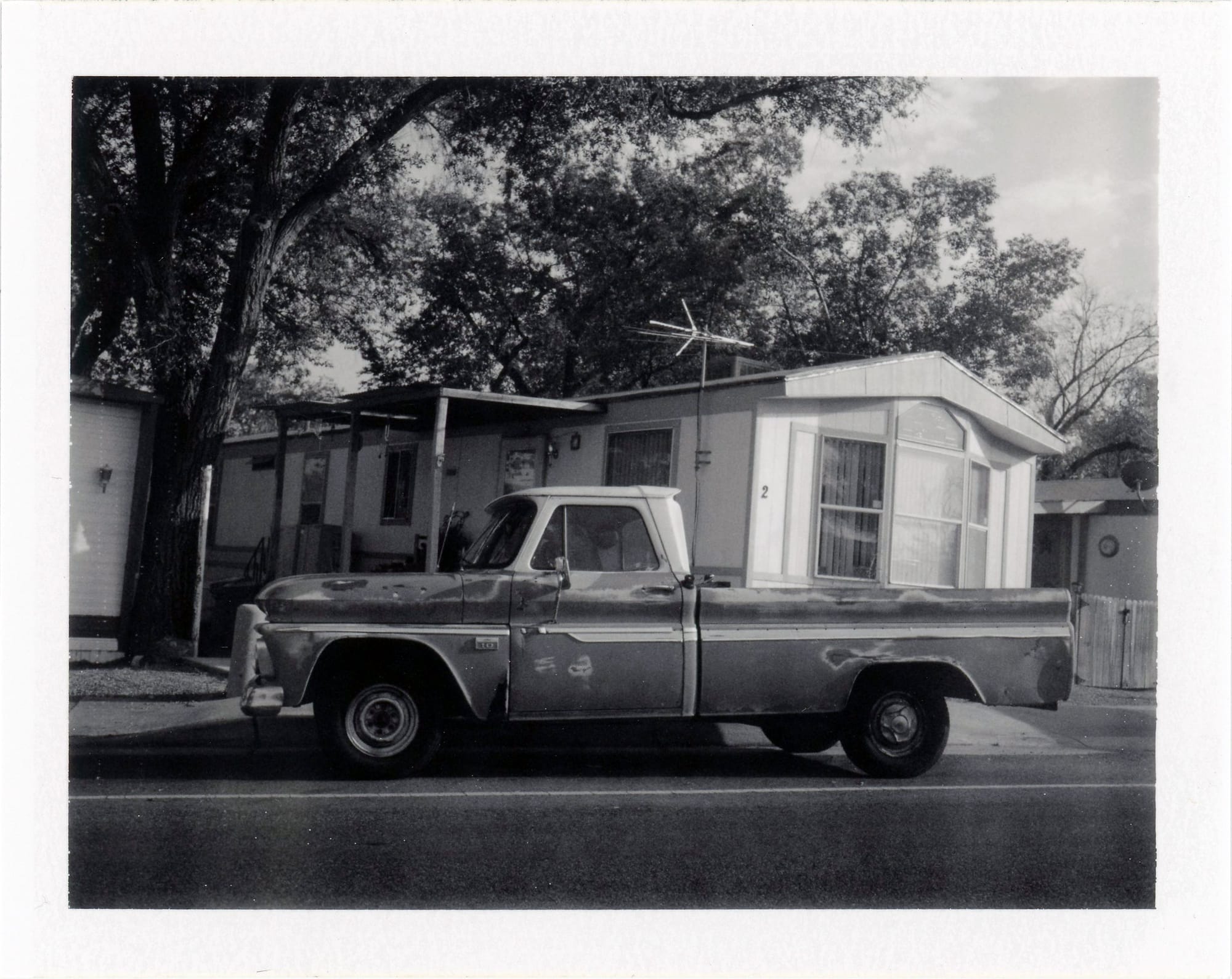 Weathered pickup truck from the 1960s parked in front of a mid-century ranch home with trees overhead.