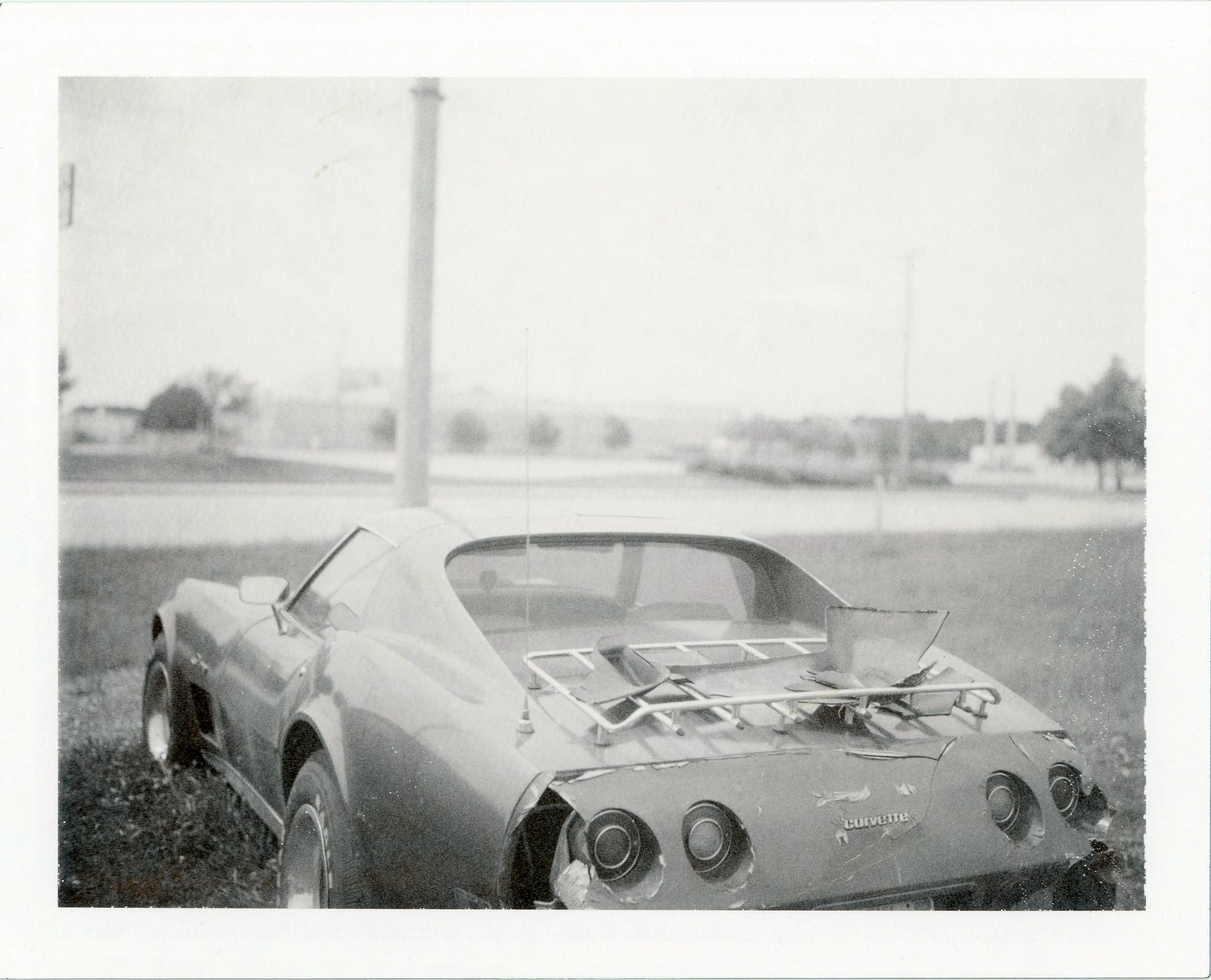 White Corvette with luggage rack and exposed engine compartment parked roadside in overcast conditions.
