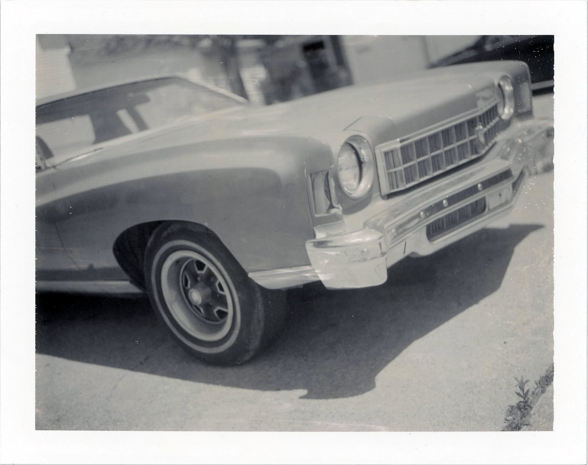 Front corner detail of vintage car showing grille, headlights and fender with soft focus background.