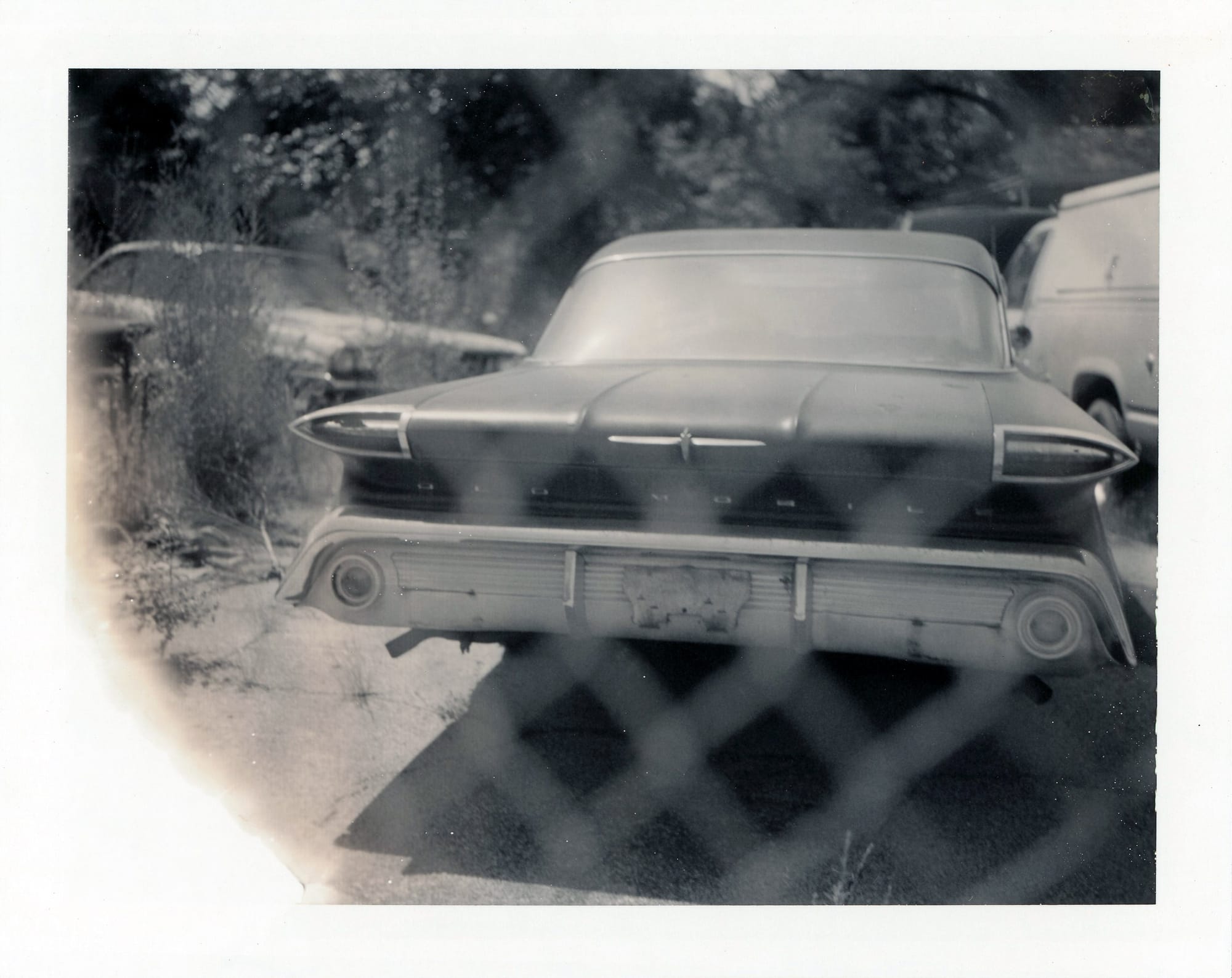 Rear view of 1950s sedan with bullet taillights and chrome bumper showing deteriorated condition.