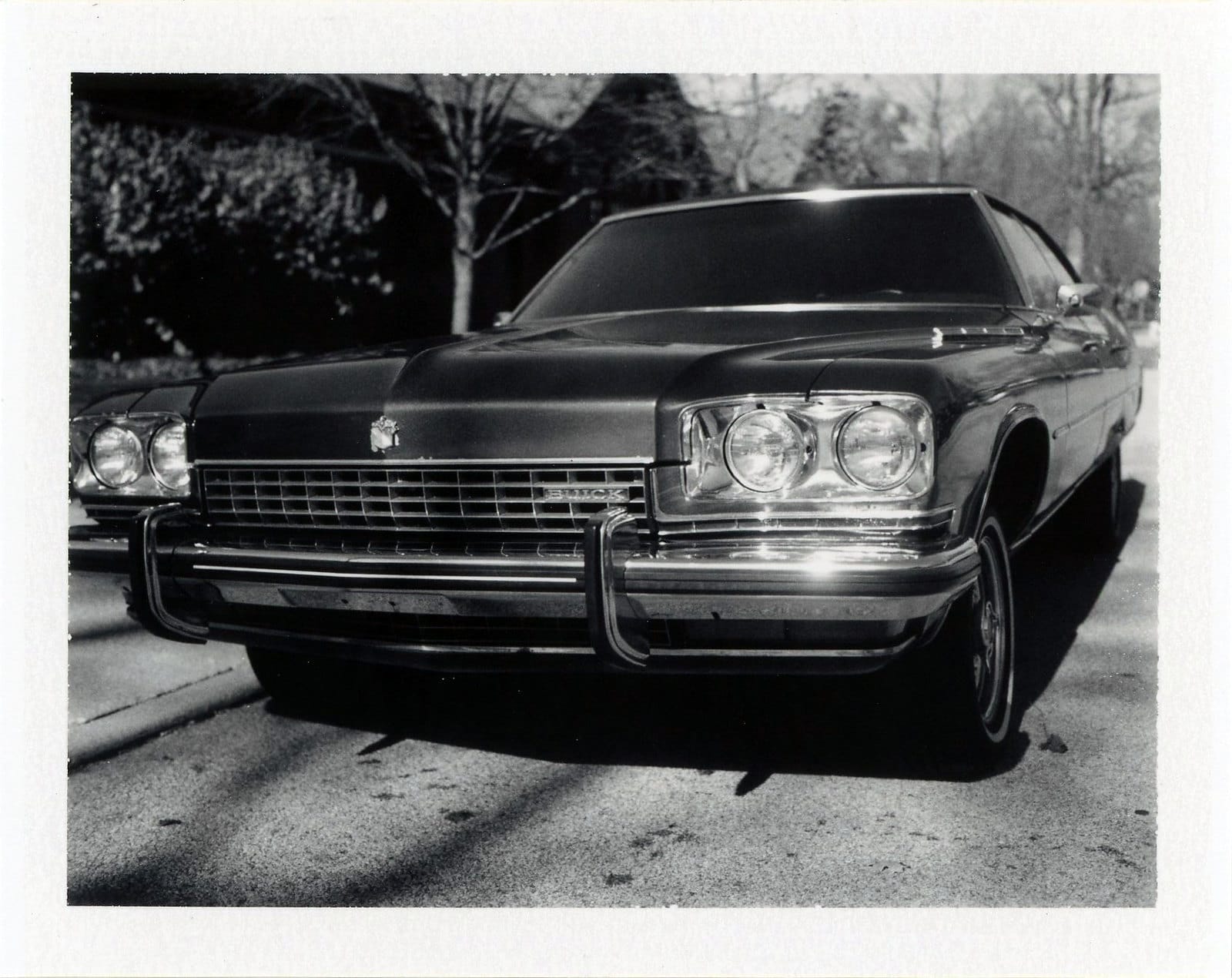 Low-angle front view of 1970s Buick with stacked headlights and chrome bumper on residential street.