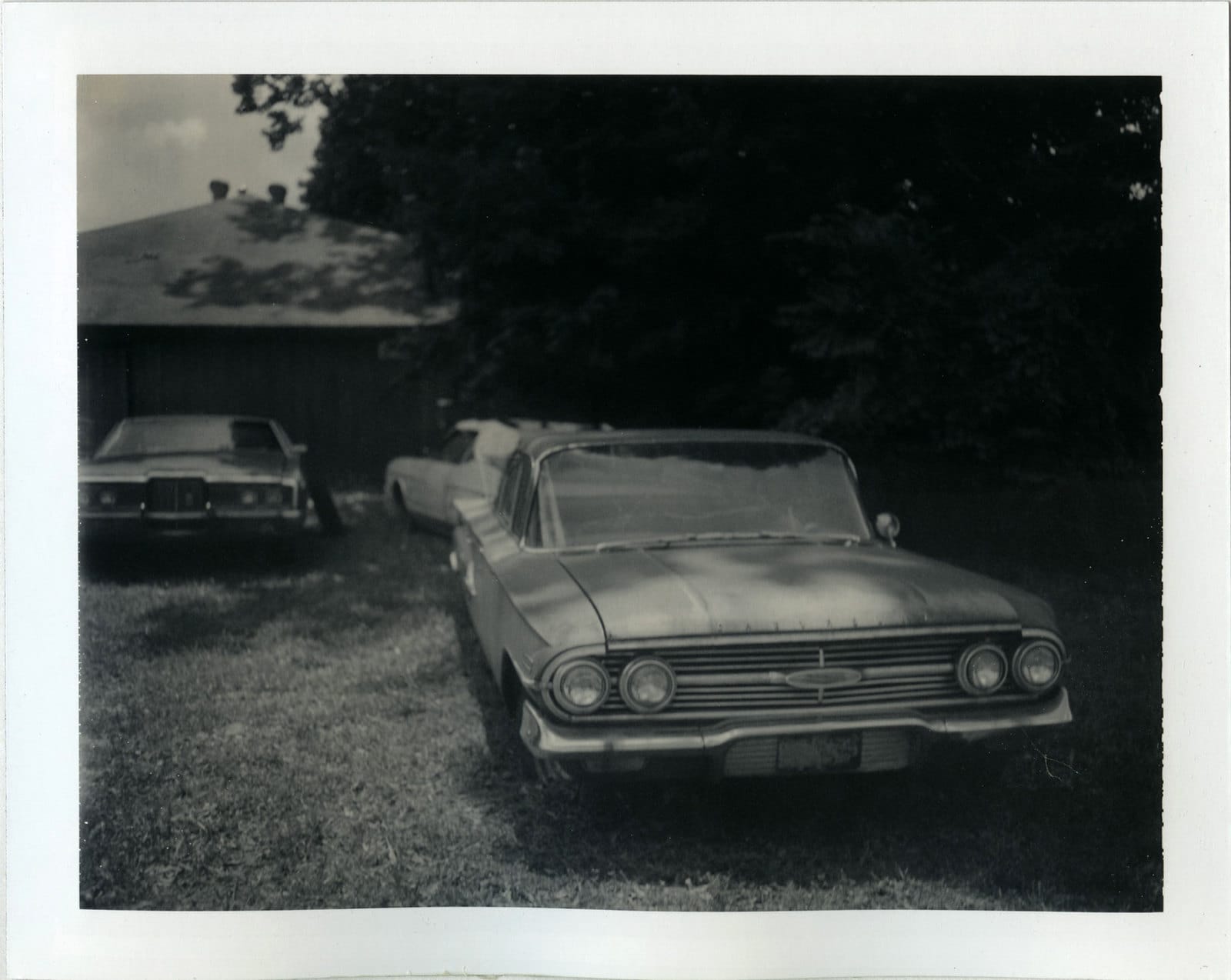 Early 1960s sedan with dual headlights and horizontal grille parked on grass with other vehicles visible.