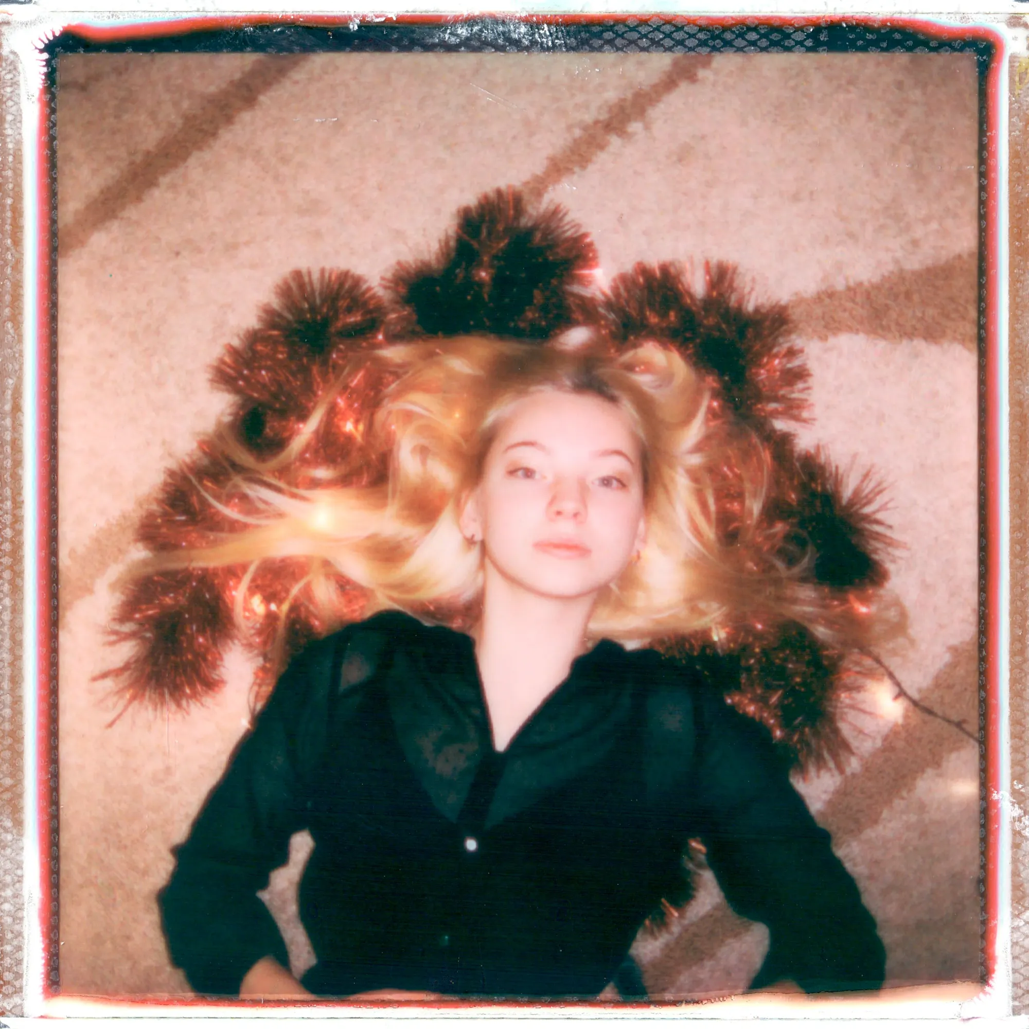 Polaroid of a girl with blonde hair and a black top, laying on the floor.