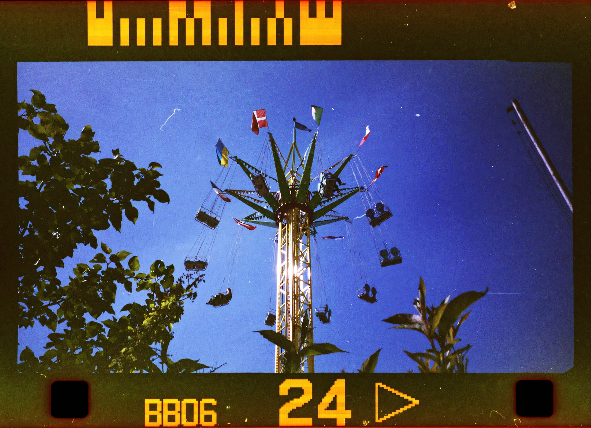 Swing ride at an amusement park with flags, against a clear blue sky.