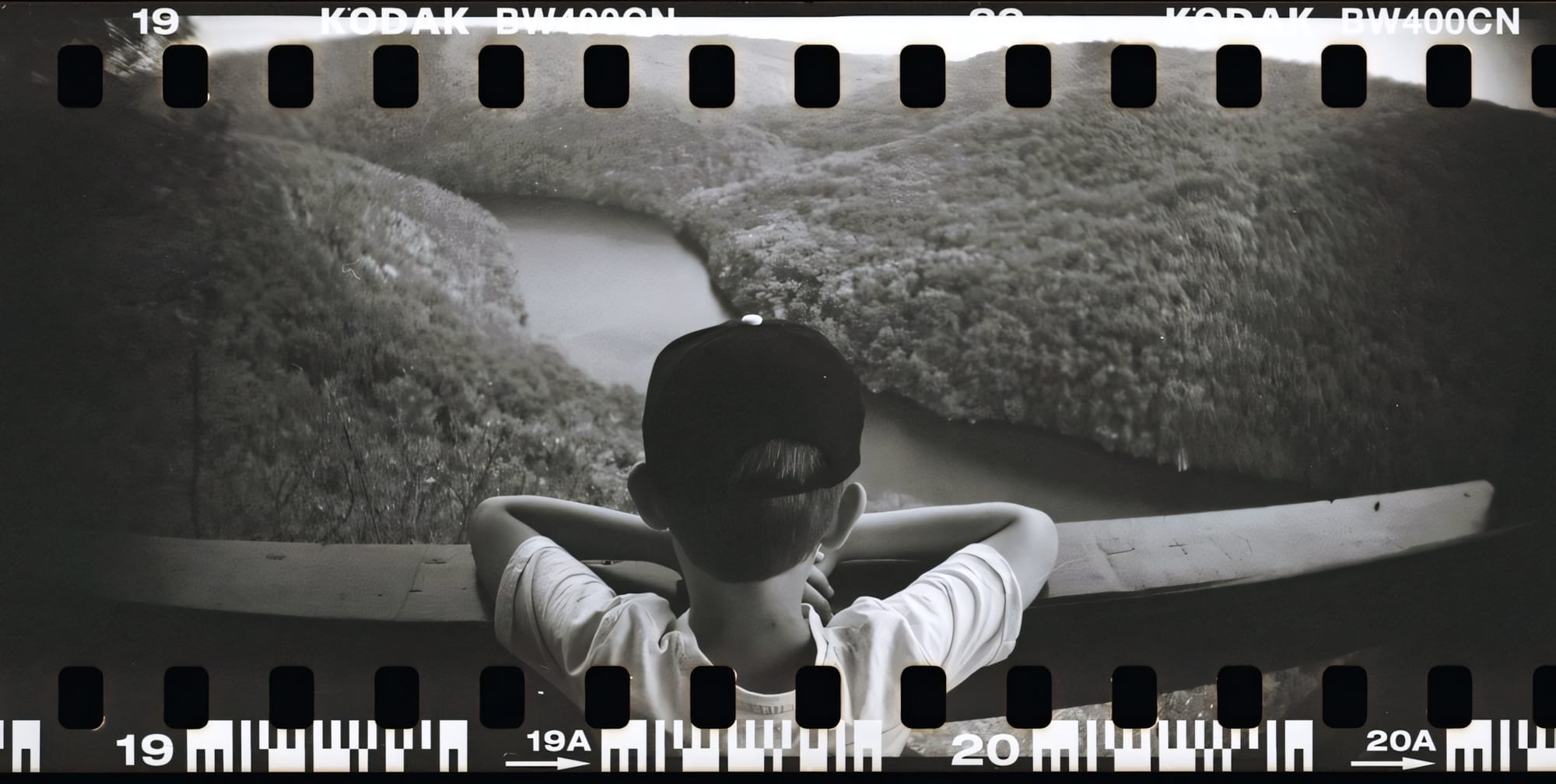 Kid standing on a high bridge looking down at a river in a valley.