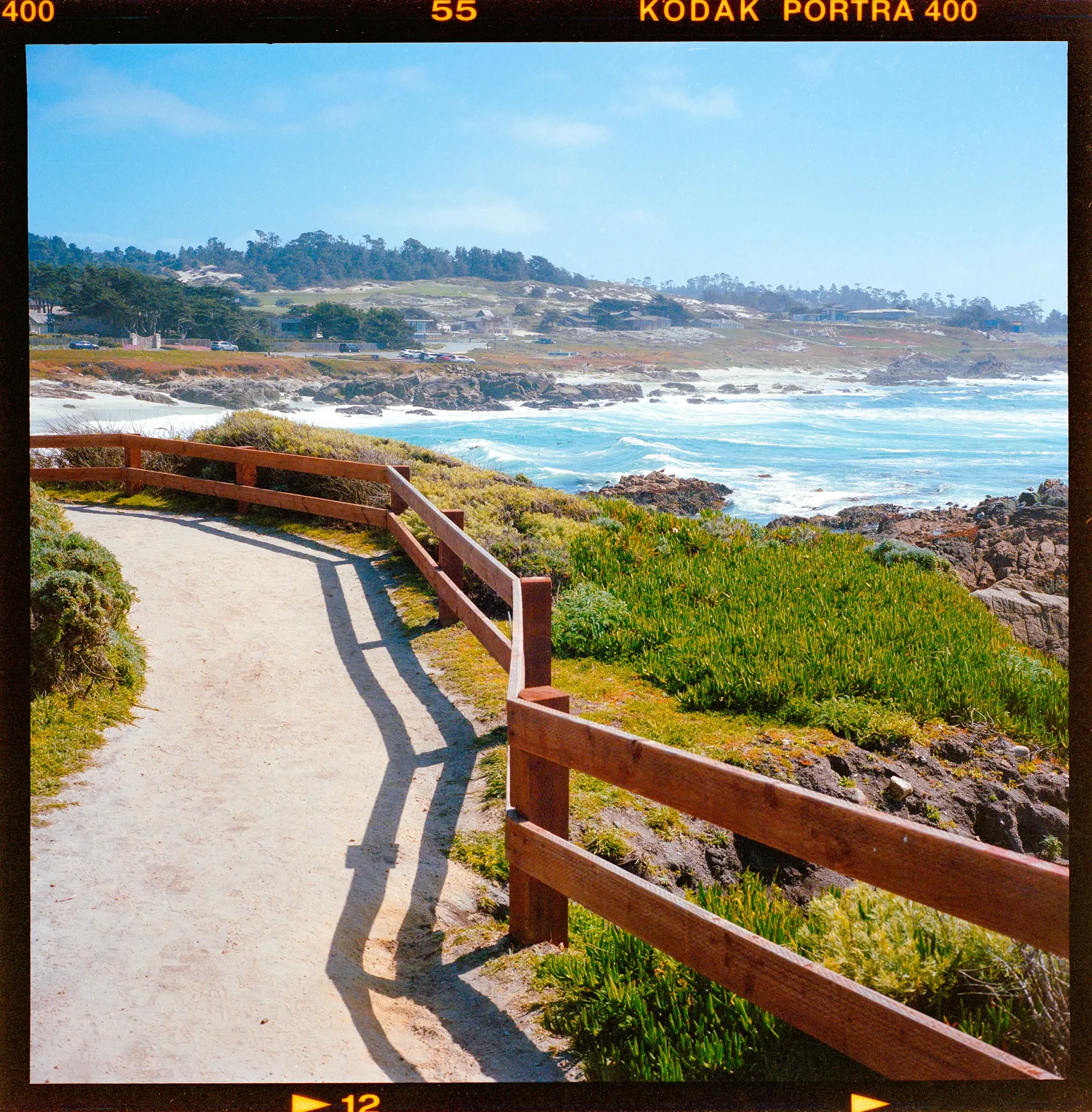 Coastal boardwalk with wooden fence overlooking Pacific Ocean and rocky shore.