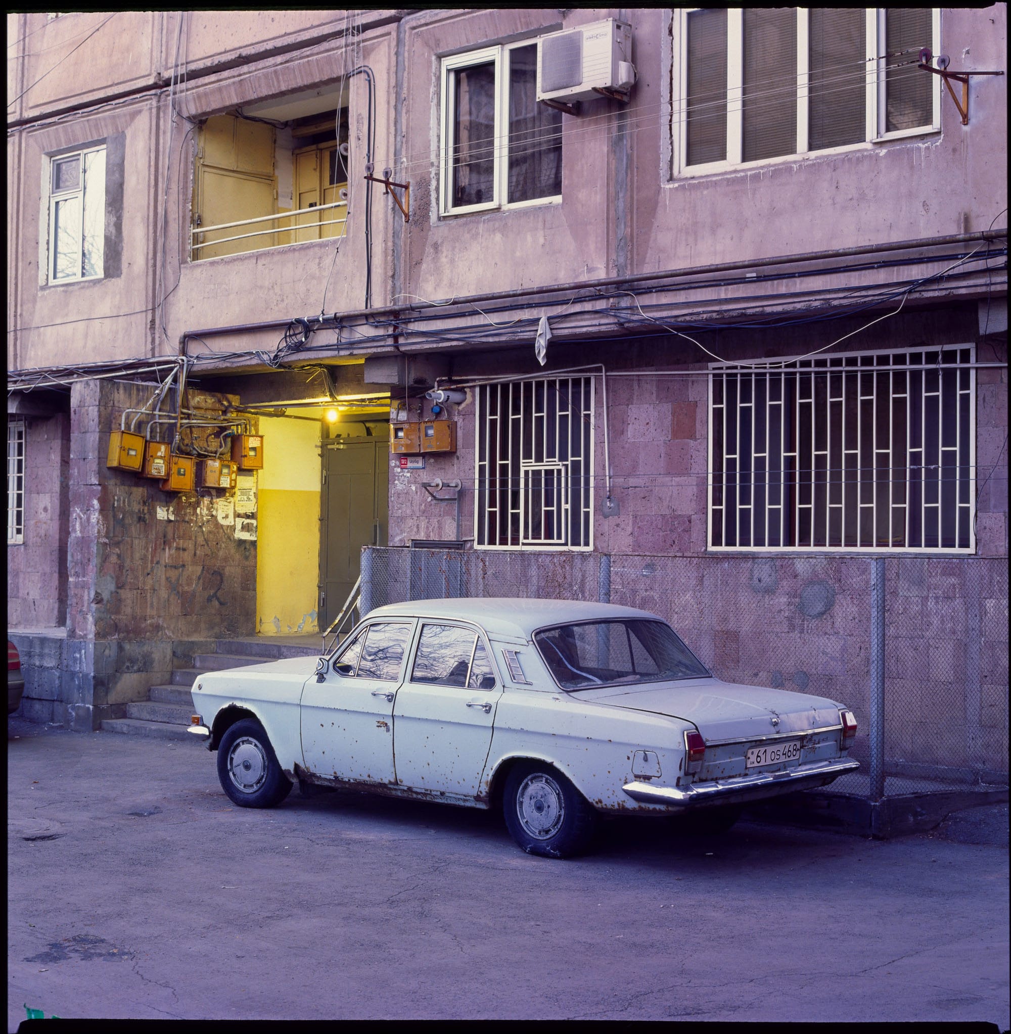 Old Soviet car parked in front of a dilapidated building.