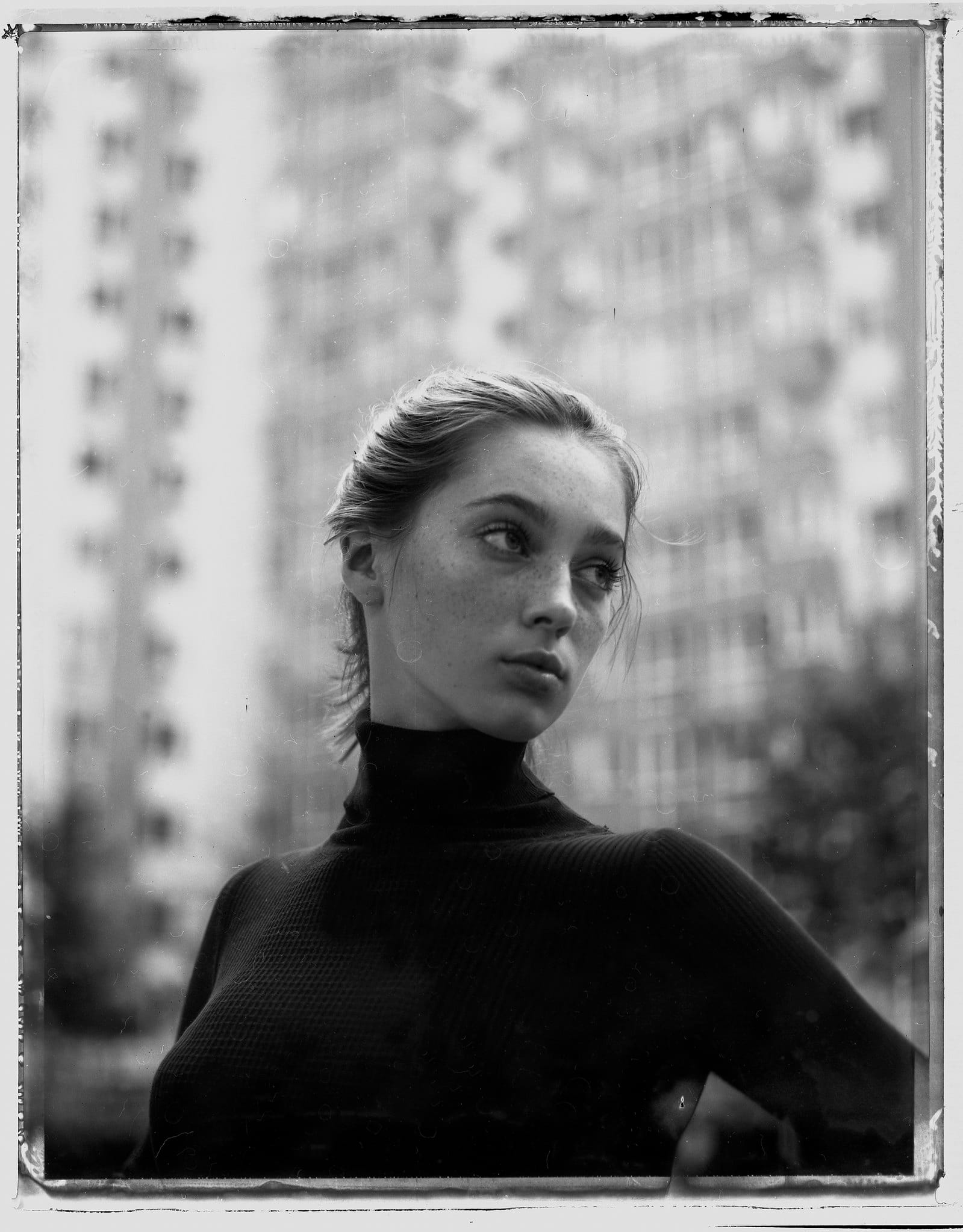 Model in black turtleneck against blurred urban backdrop on large format film.