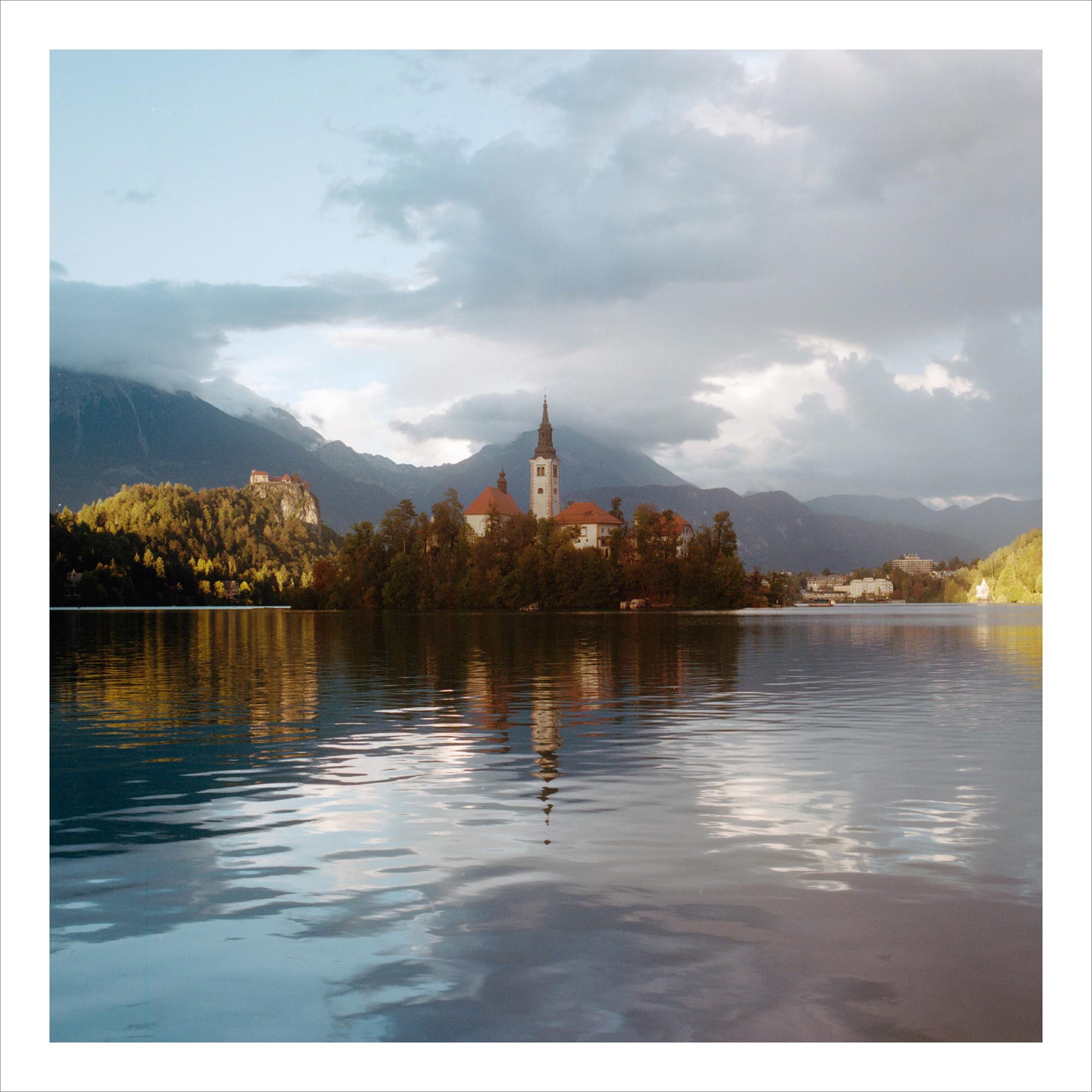 Serene view of Lake Bled, surrounded by mountains and autumn foliage.