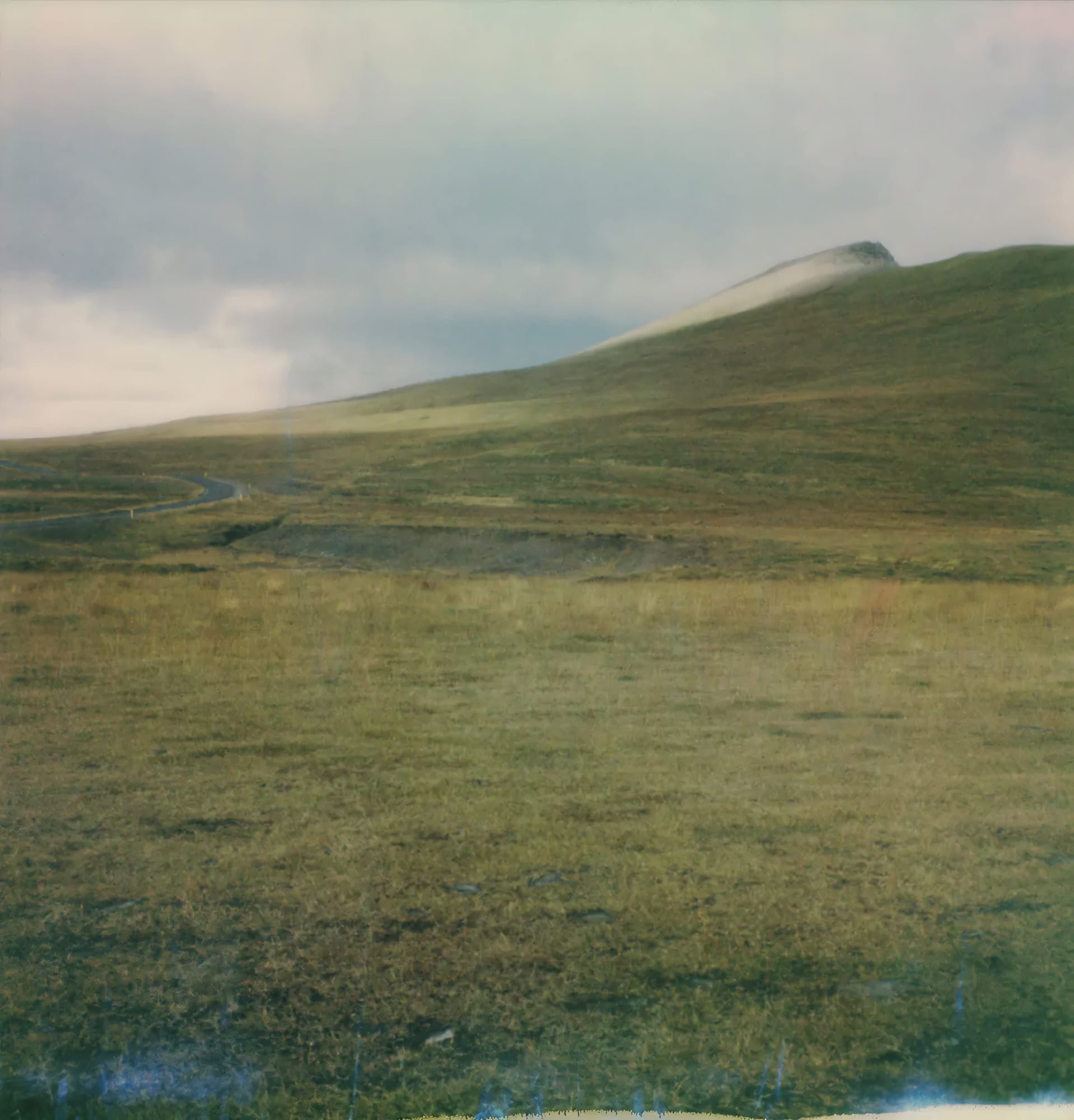 Rolling grassland with distant hill and overcast sky on film.