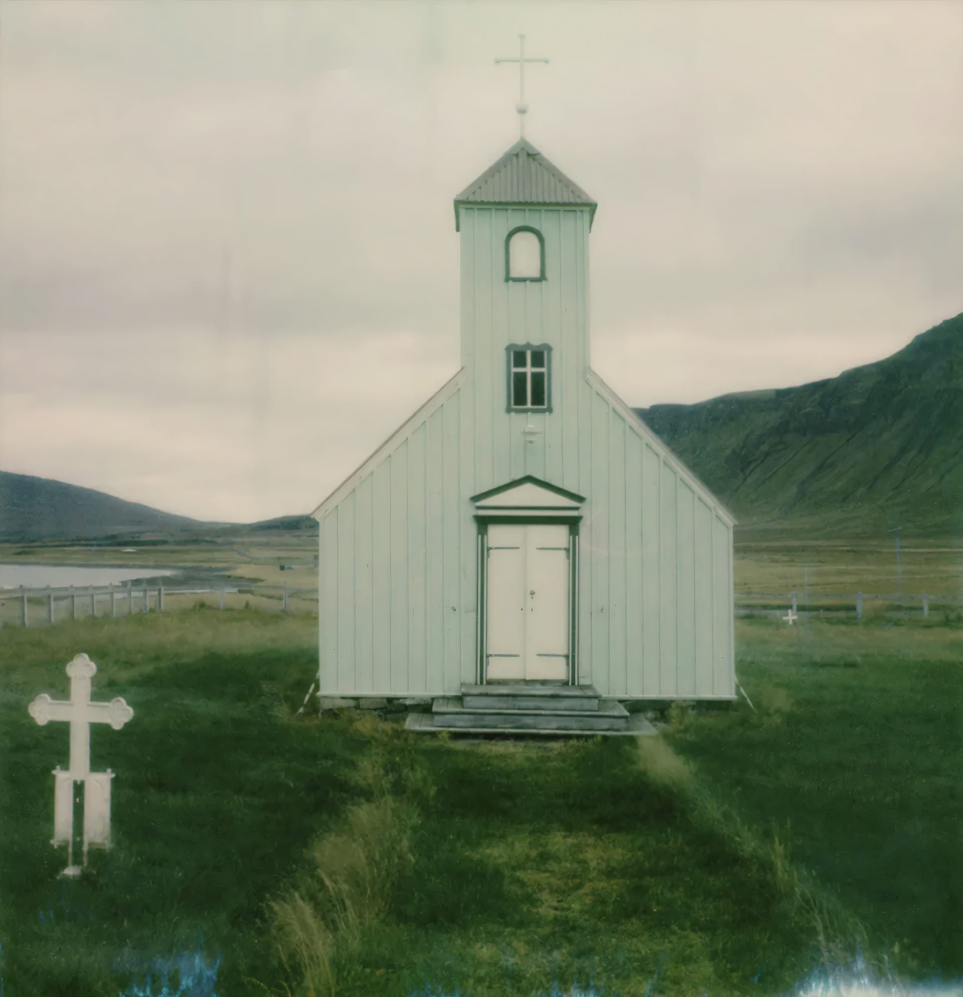 Small white church with bell tower and cross in Icelandic valley on Polaroid.