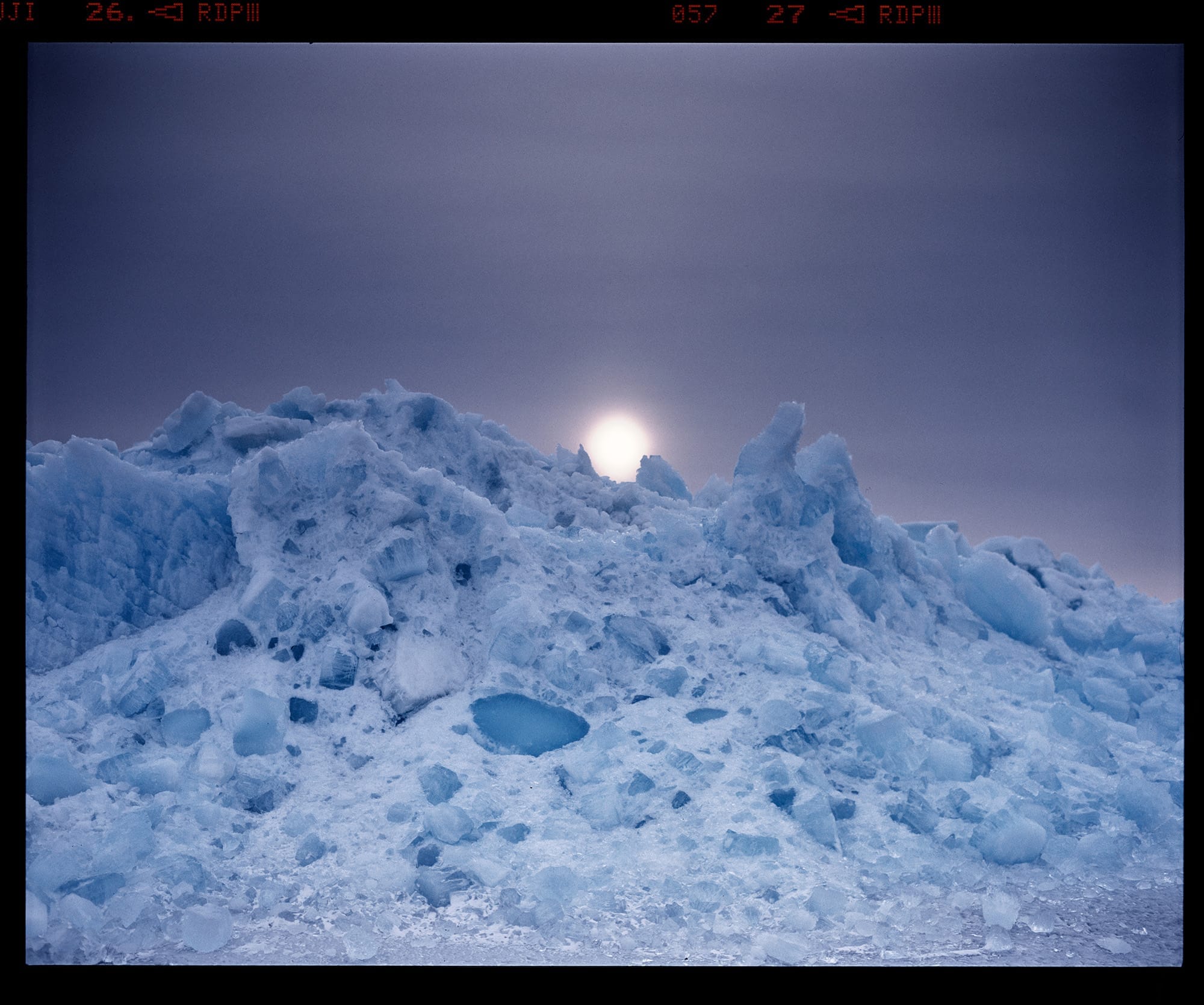 Jagged ice formation with sun centered behind frozen peak creating glow, frame numbers visible in border.
