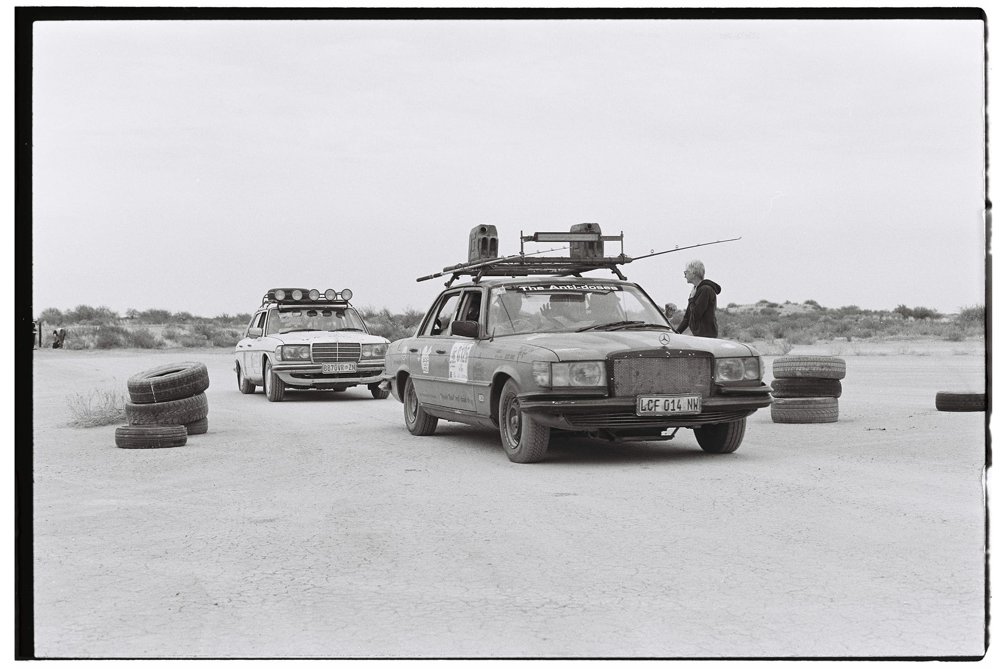 Mercedes sedans with roof racks at tire markers on dirt track.