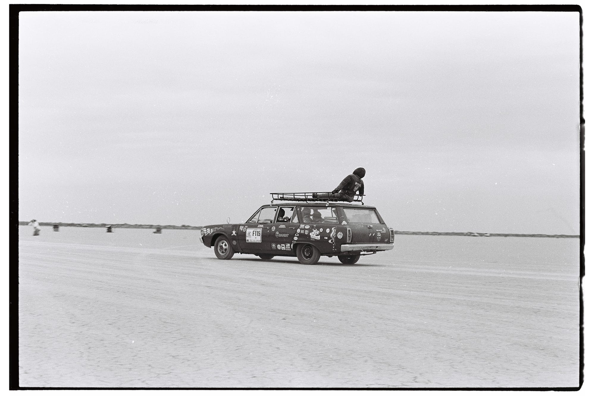 Station wagon with dummy on roof rack crossing salt pan.