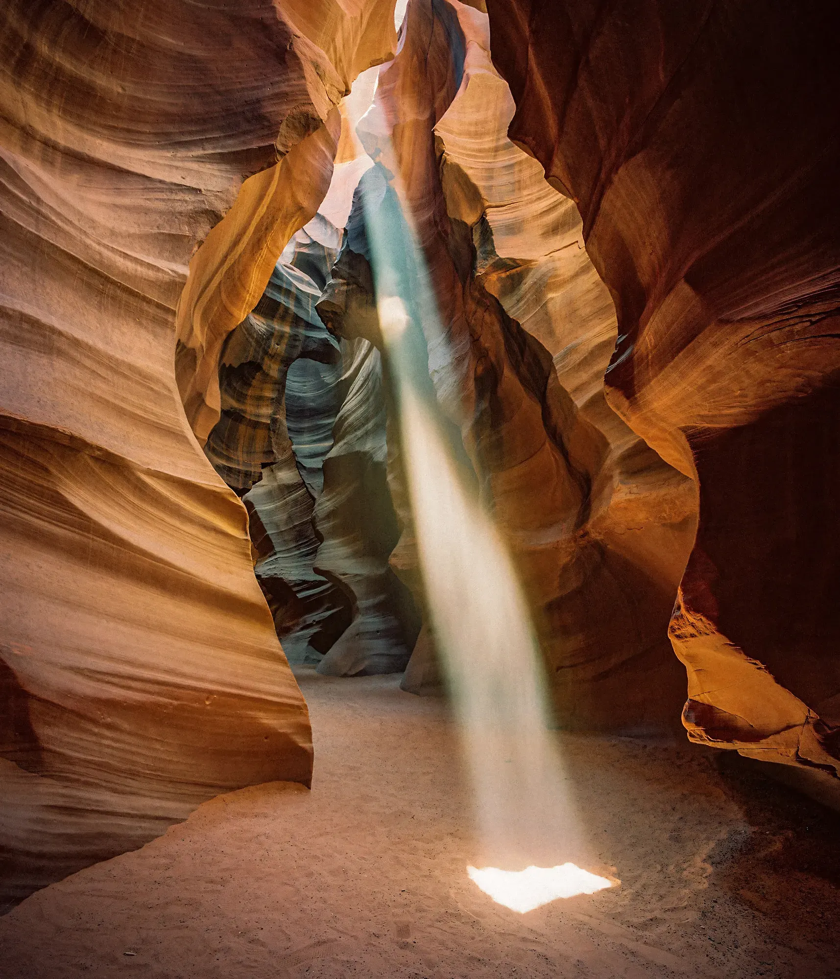 Sandstone slot canyon with light beam streaming down onto orange and blue striated rock walls.