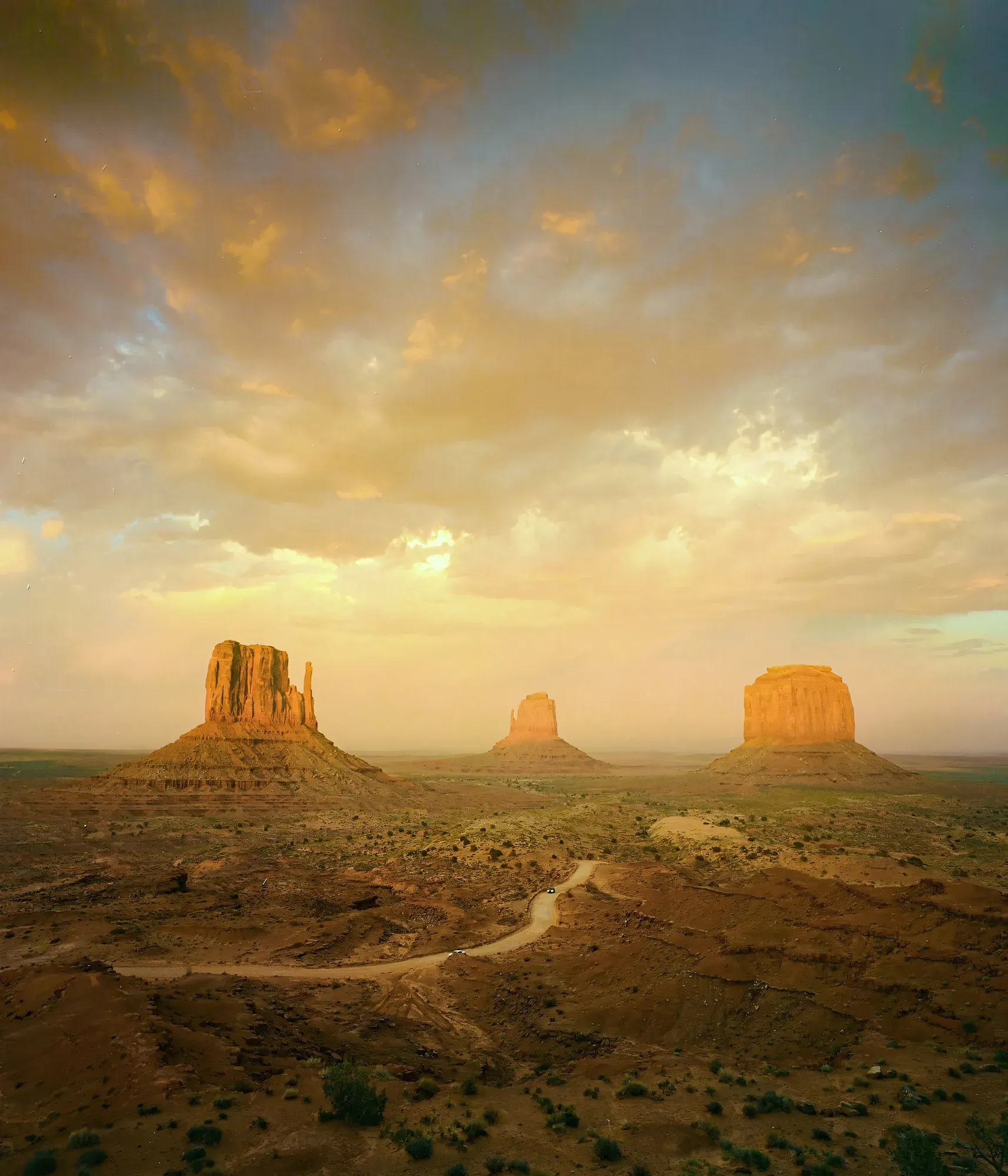 Three sandstone buttes of Monument Valley under golden light with winding dirt road through desert.