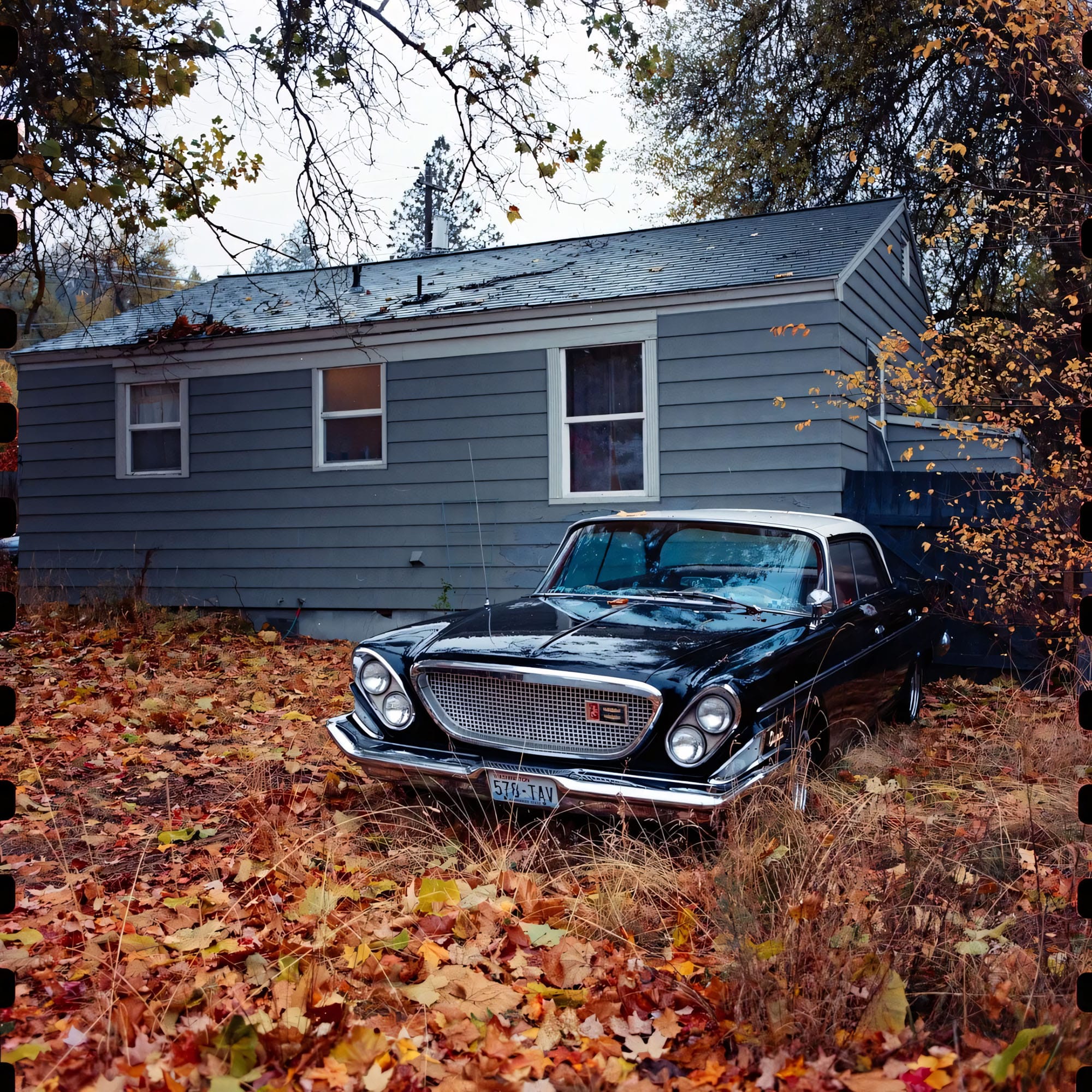 Vintage car parked in front of house covered in fallen autumn leaves.