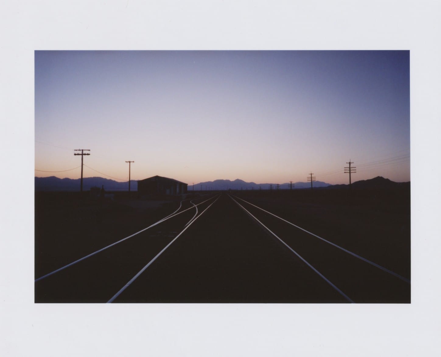 Railroad tracks at dusk with telephone poles and mountains.