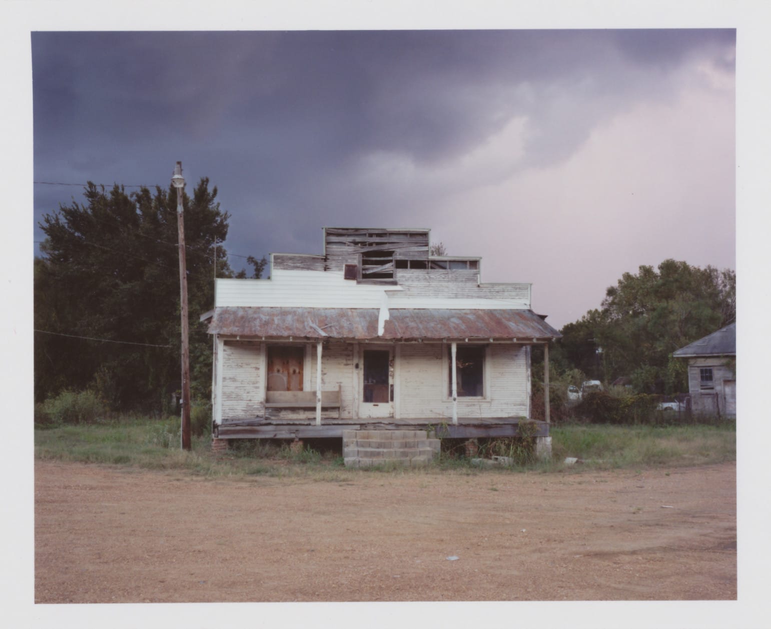 Abandoned white house with collapsed roof and porch.