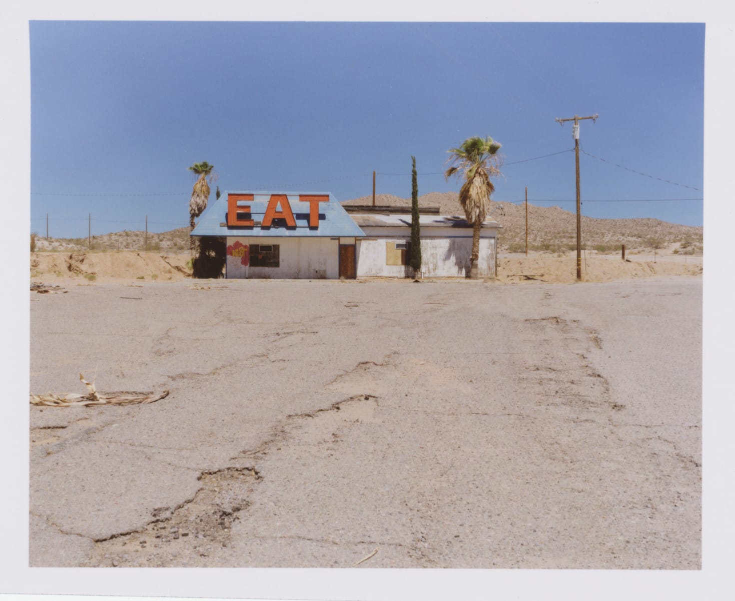 Abandoned diner with "EAT" sign in desert.