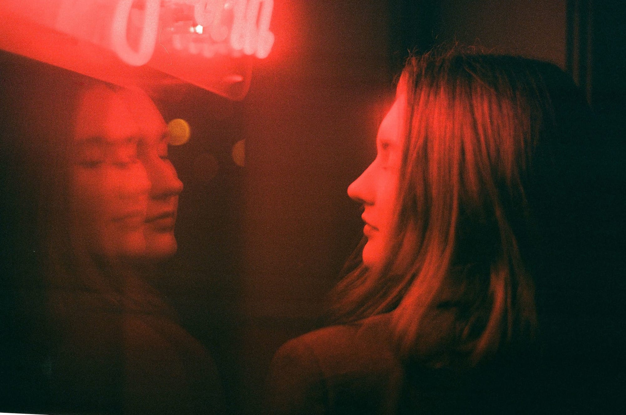 Brunette beauty reflects on glass under red neon glow in dark interior.