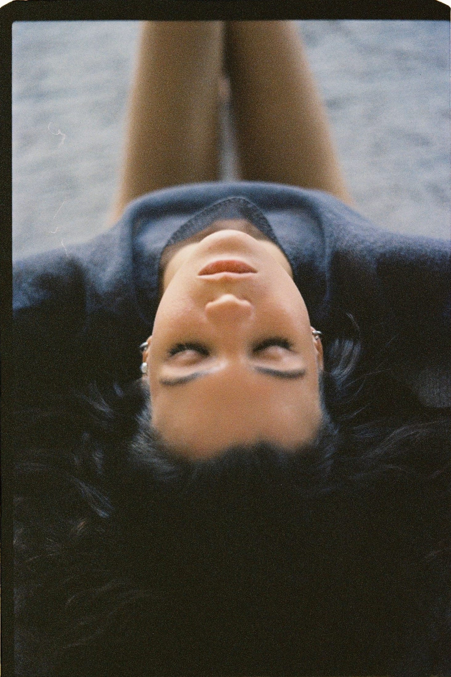 Overhead view of woman lying on dark surface with legs extended upward.