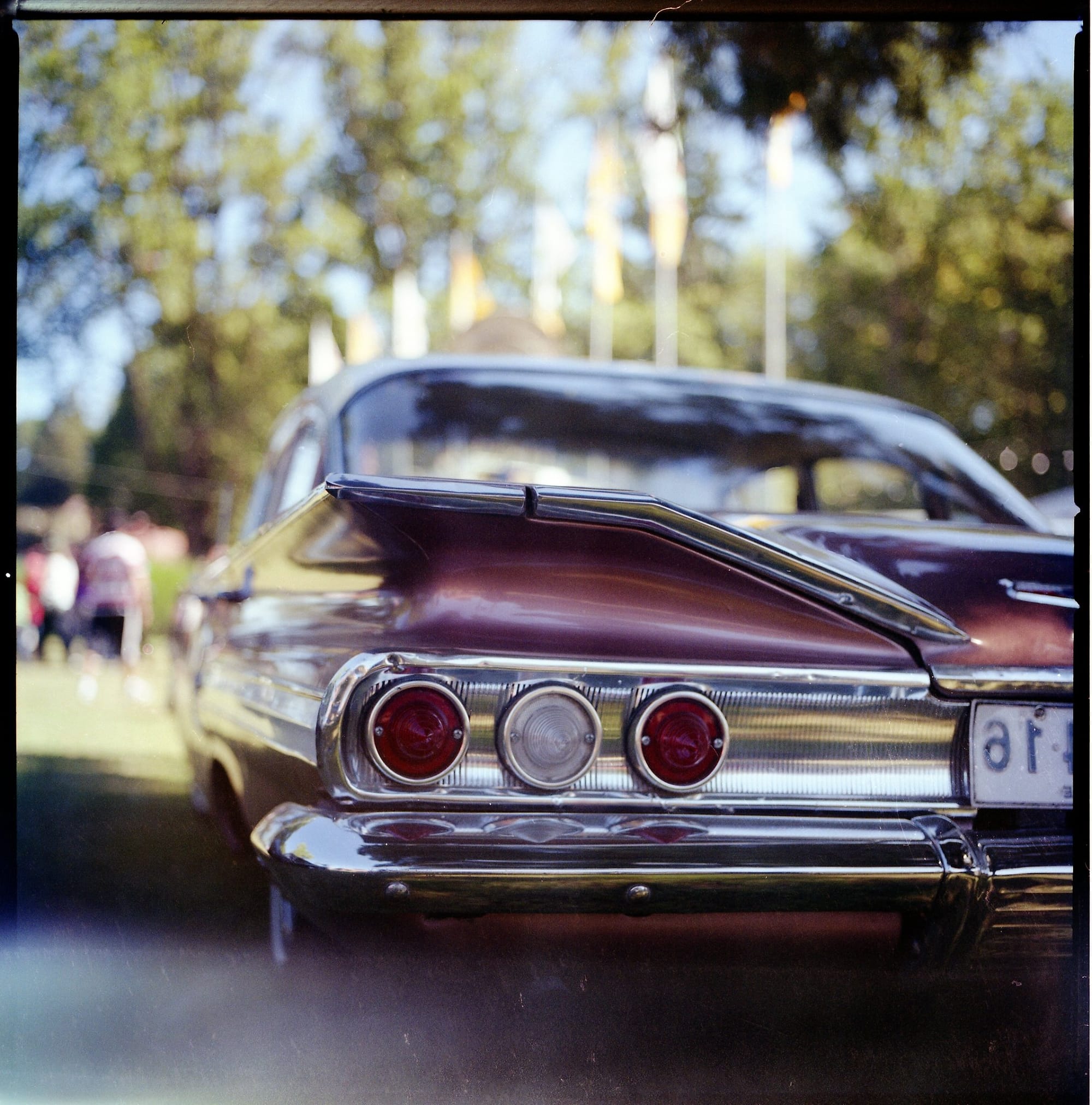 Classic car chrome tail lights and fins close-up detail at outdoor car show with blurred background.