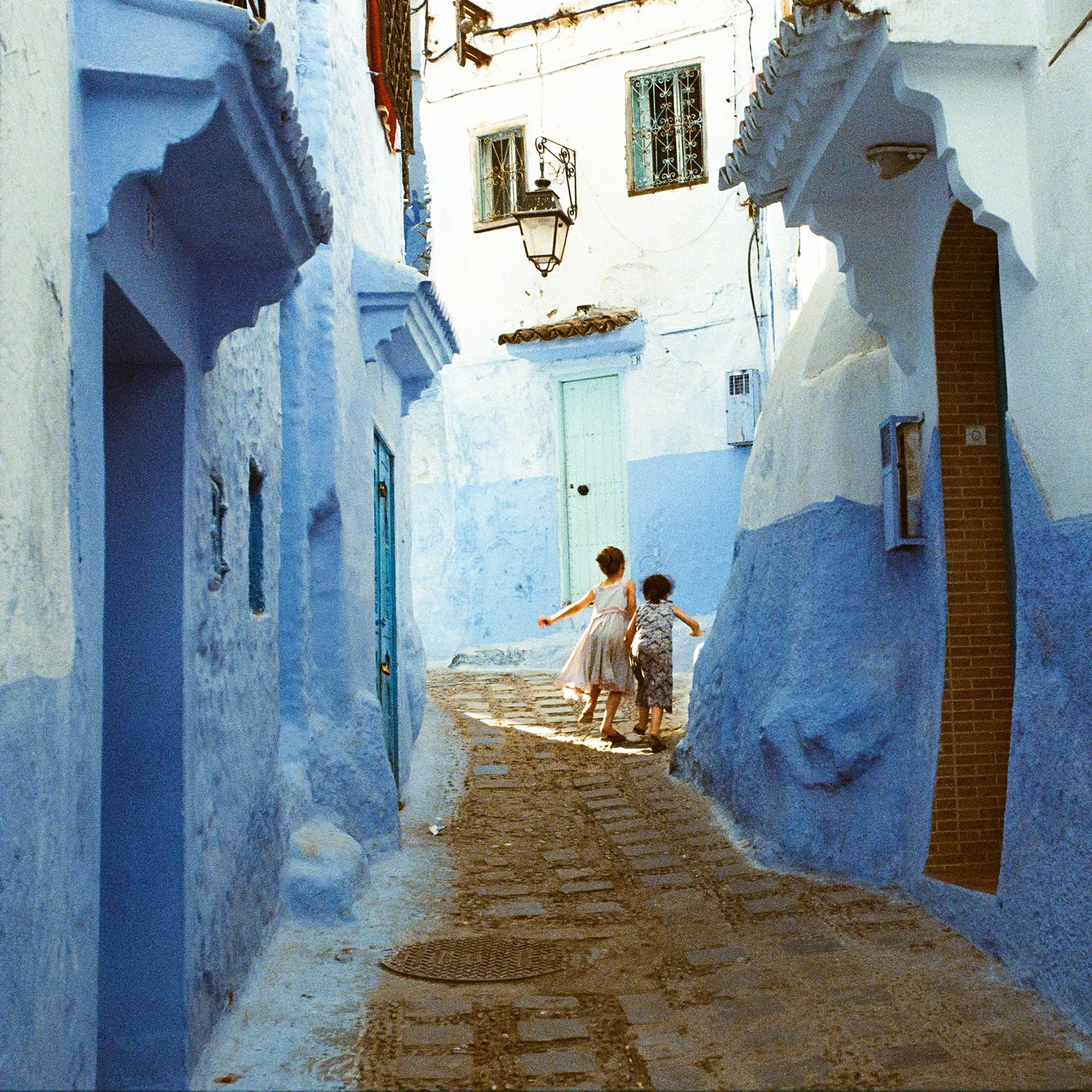 Children running through narrow blue-painted alleyway in Chefchaouen, Morocco.