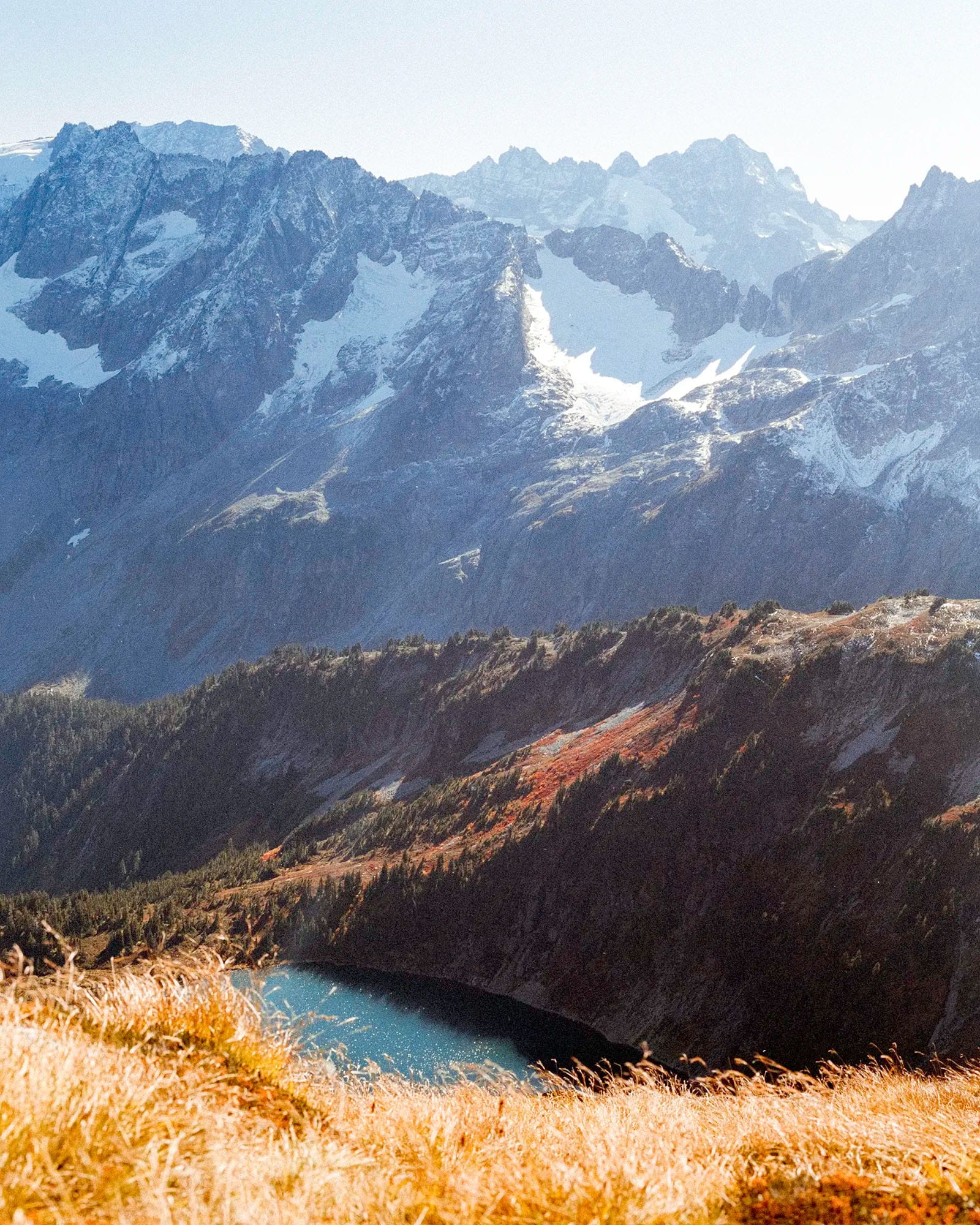 Snow-capped mountain peaks with turquoise alpine lake surrounded by autumn-colored hillside and golden grasses.