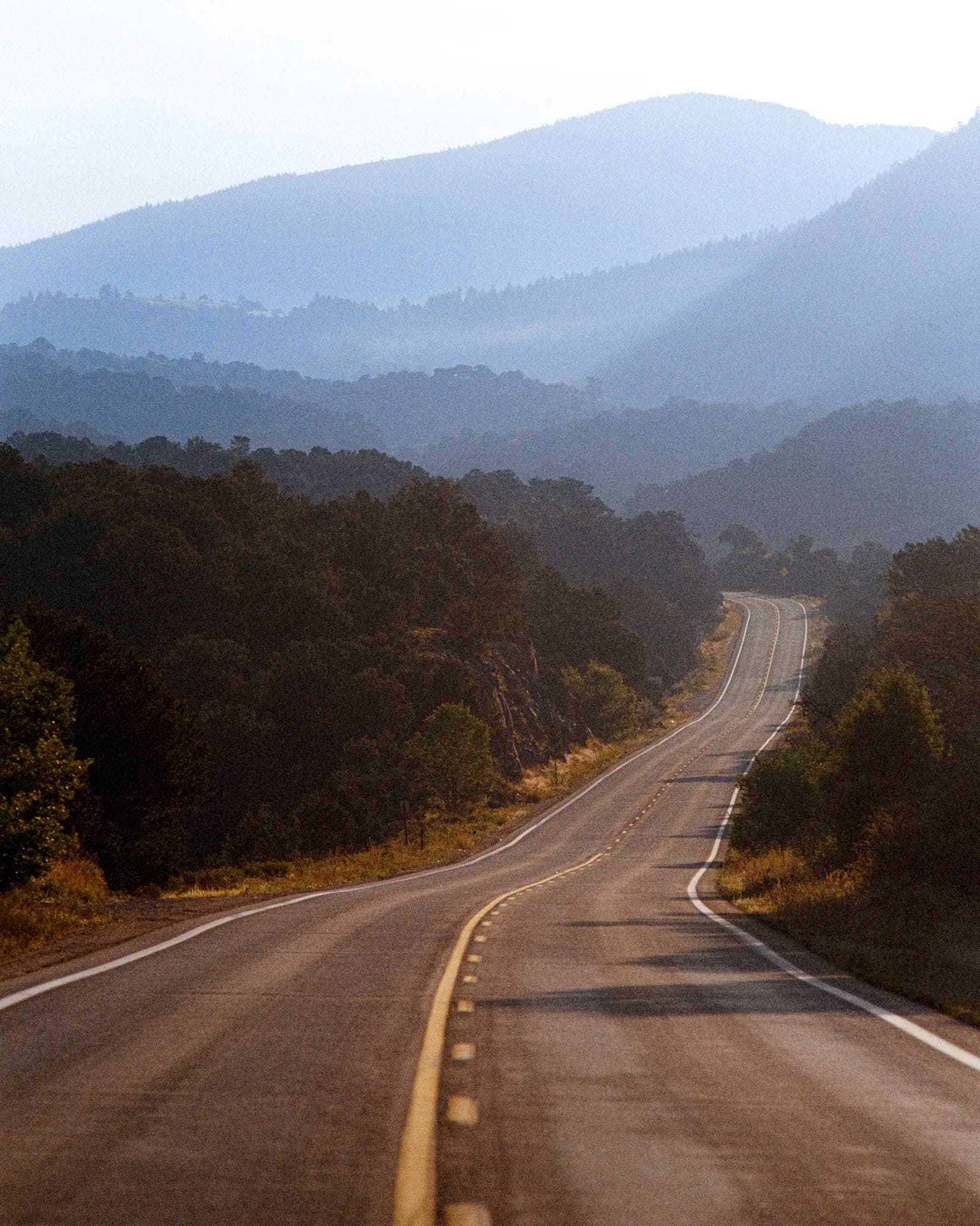 Winding mountain highway disappearing through forested hills into misty blue distance.