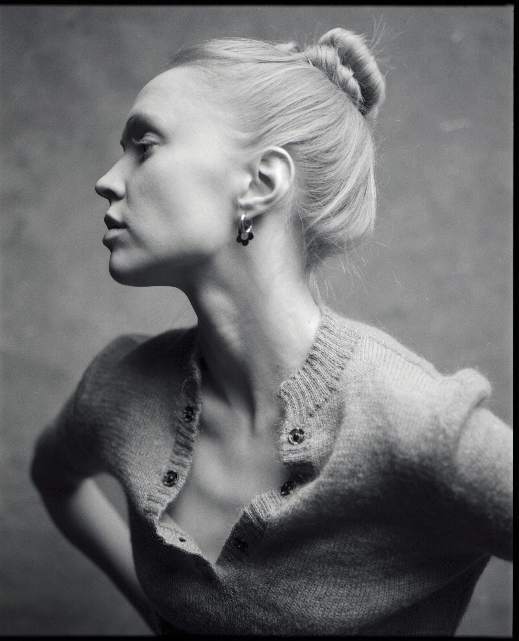 Profile portrait of woman with hair pulled back in cardigan against gray backdrop.