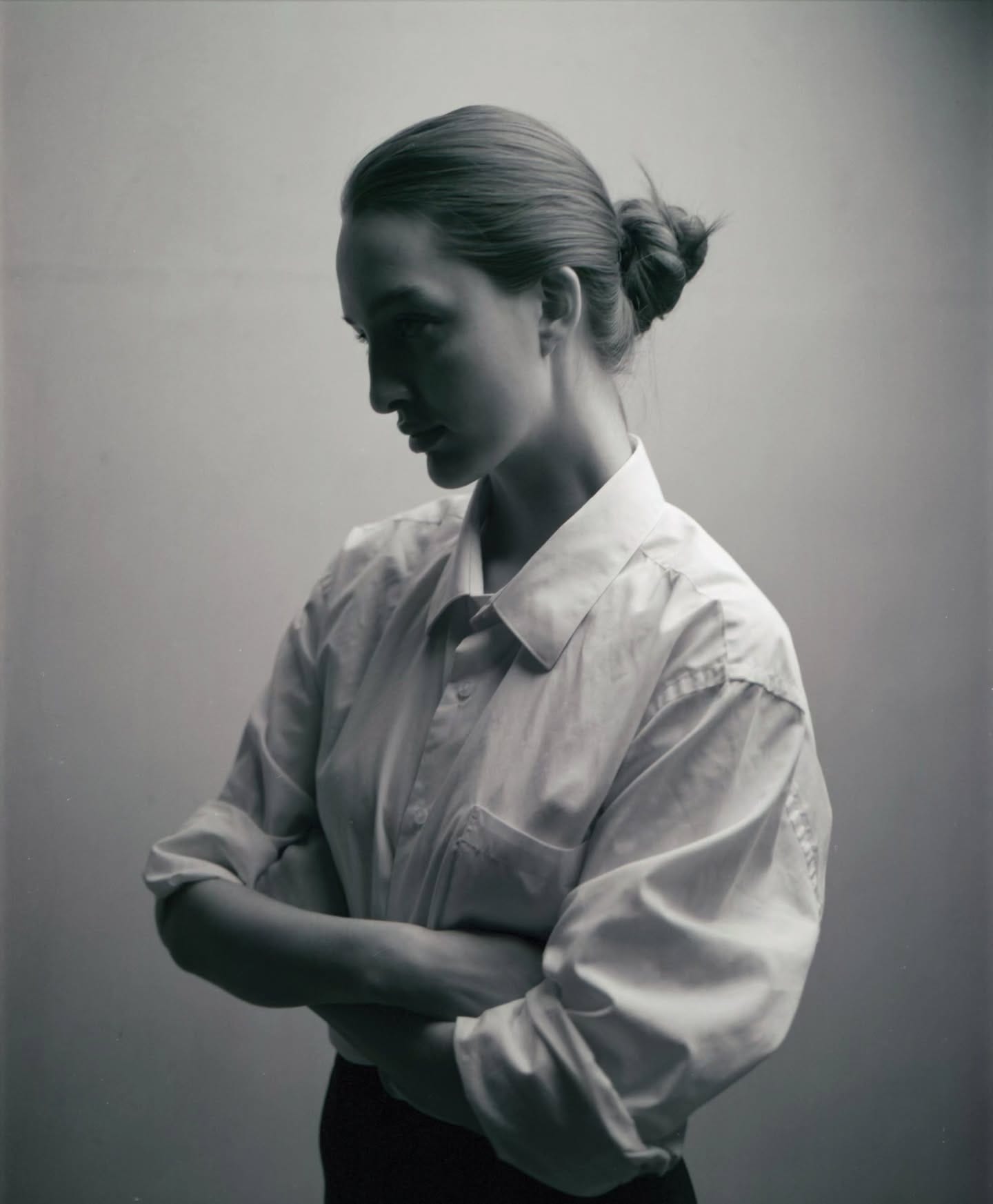 Profile portrait of woman in white button-up shirt with arms crossed against gradient background.