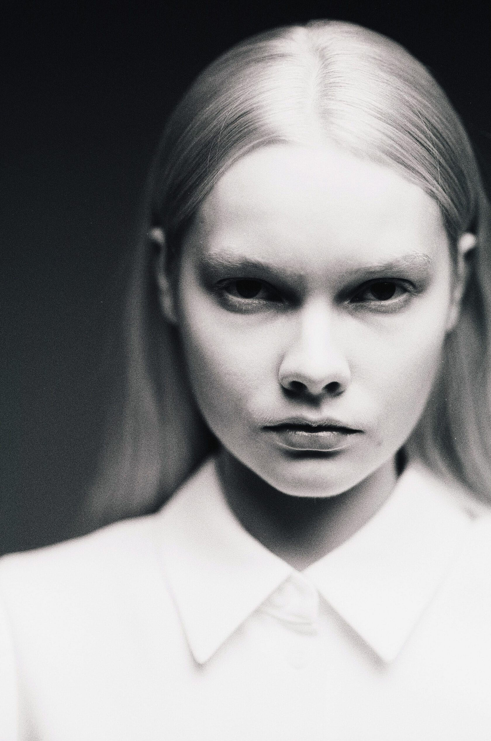 Woman with center-parted hair and dramatic eye makeup in white collared shirt.