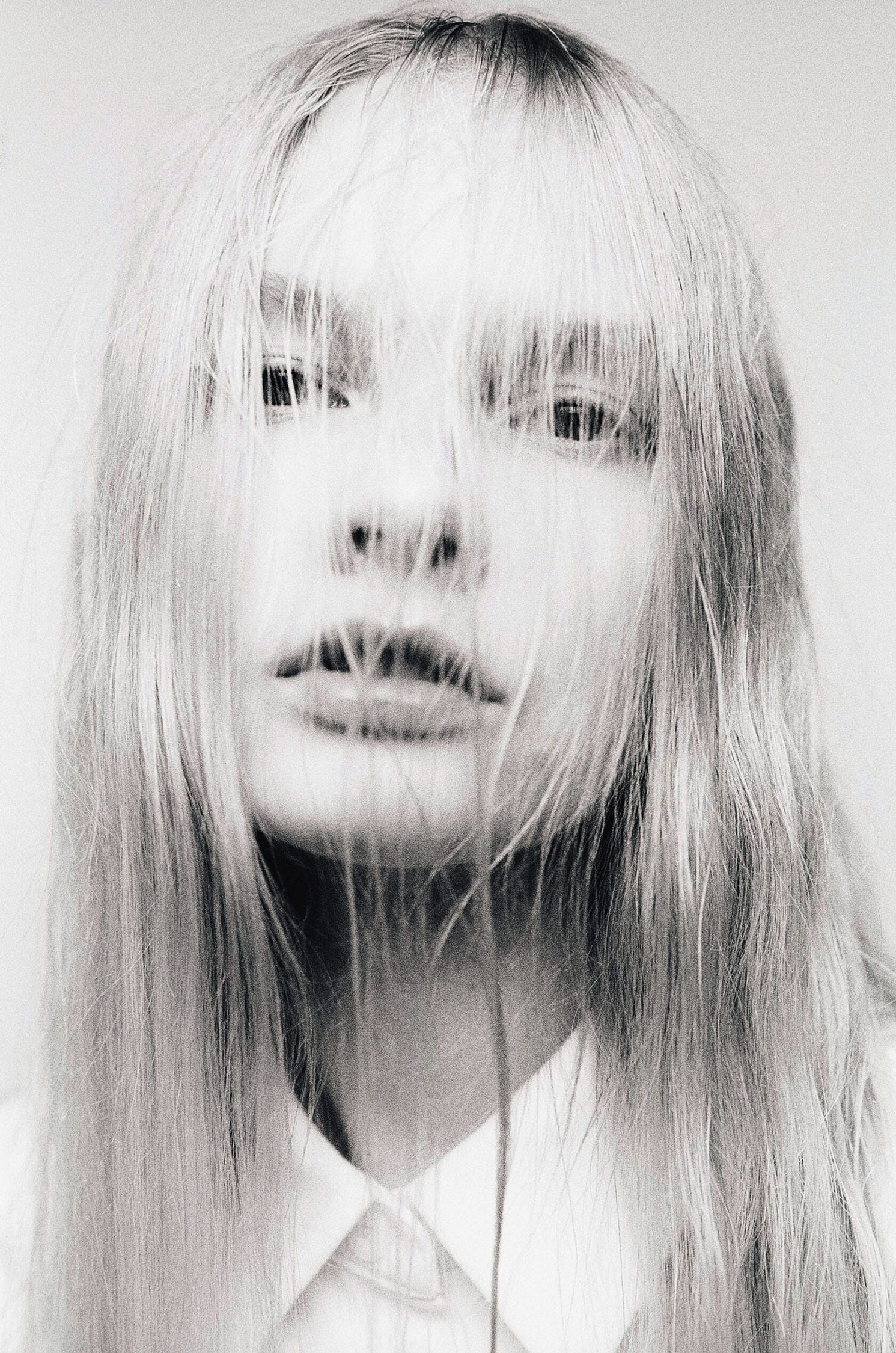 Monochrome portrait showing woman's face through blonde hair strands.